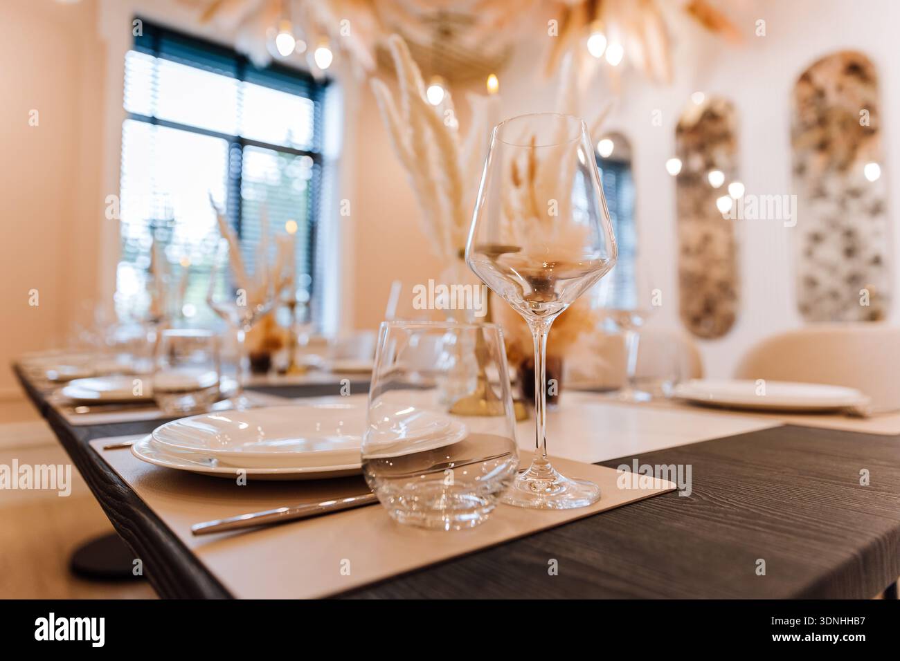 Elegant restaurant table setting with glassware, pampas decor and warm bokeh lighting Stock Photo