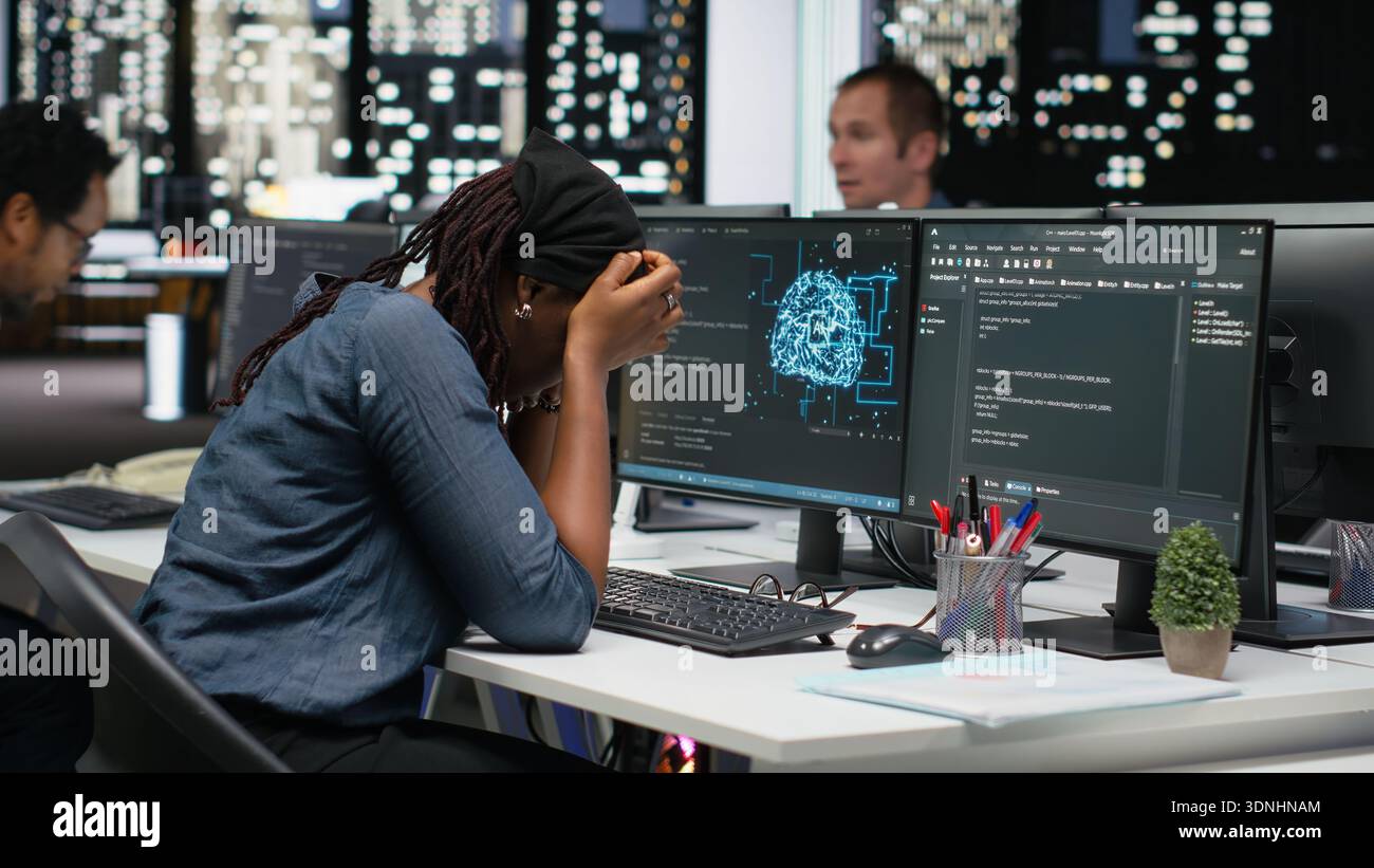 Sleepy IT specialist in office typing code on computer, developing machine learning model late at night. Tired system administrator writes programming language scripts, working overtime Stock Photo