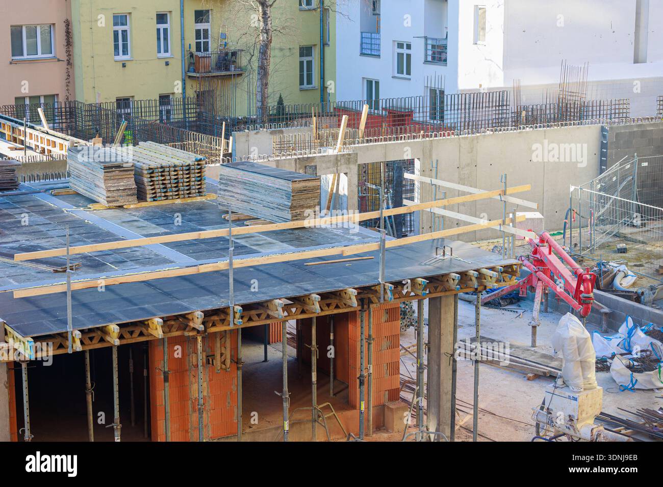 Timber Frame Rising Wall A busy construction site shows brick walls rising, timber framing, and ...