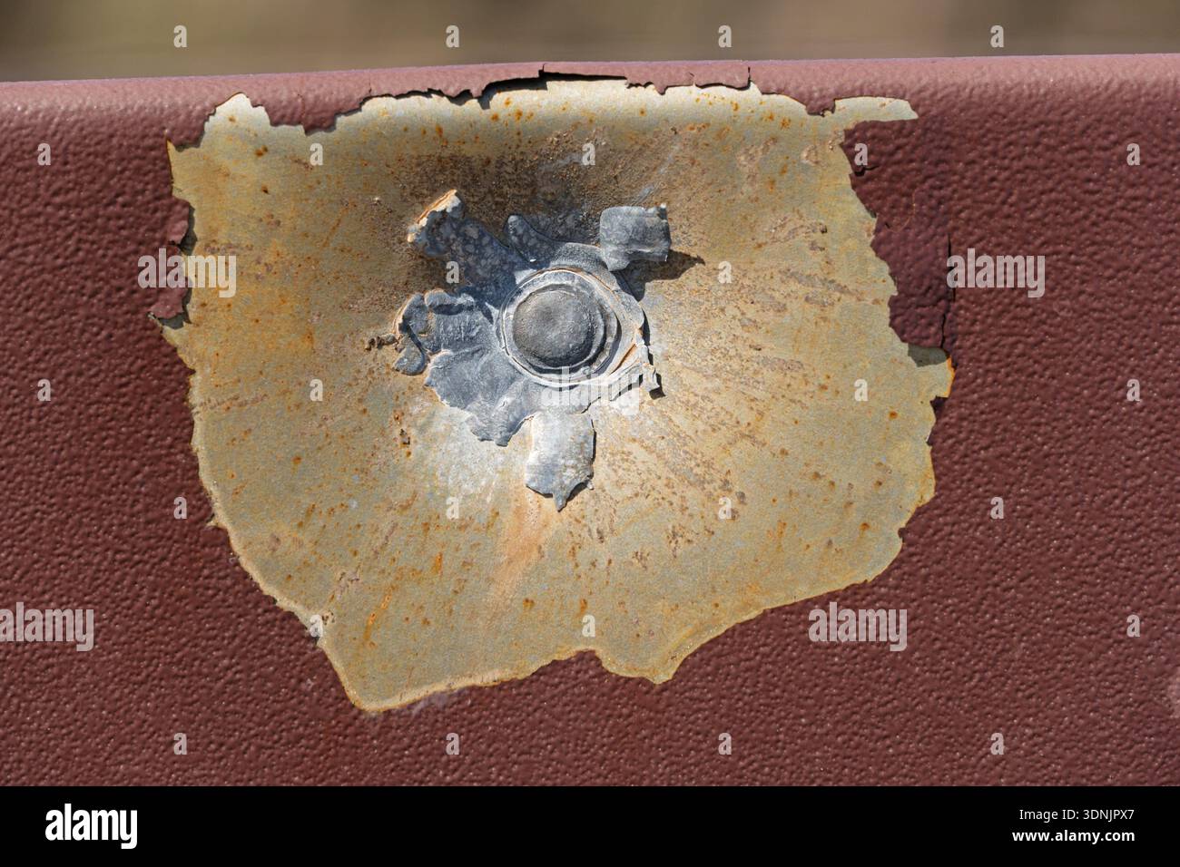 location where a lead bullet hit a painted metal sheet and blew off the paint and dented the metal with the flattened bullet still stuck at the impact Stock Photo