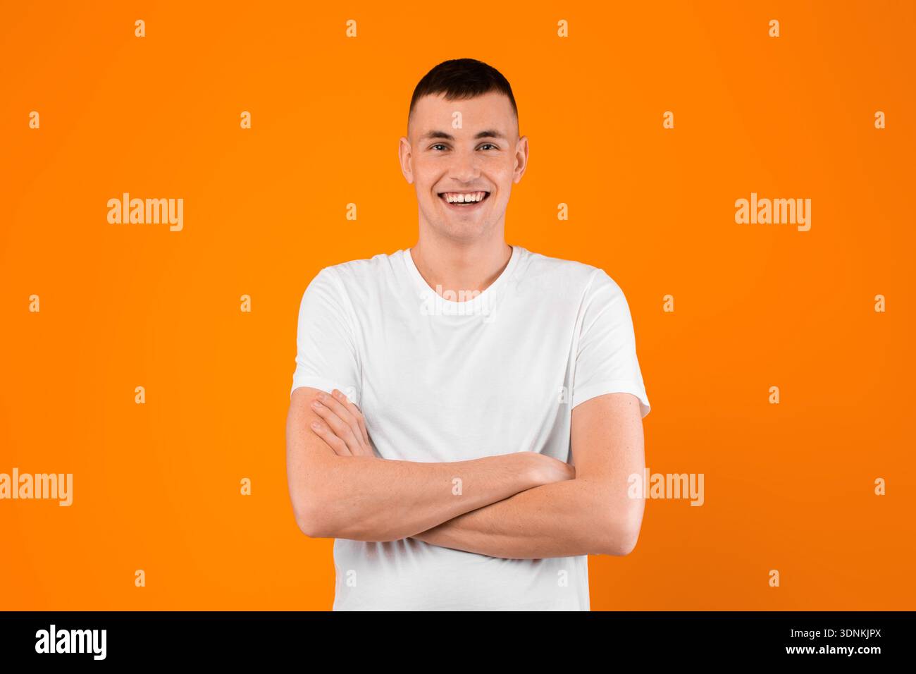 Young Man Smiling To Camera Posing Crossing Hands, Yellow Background Stock Photo