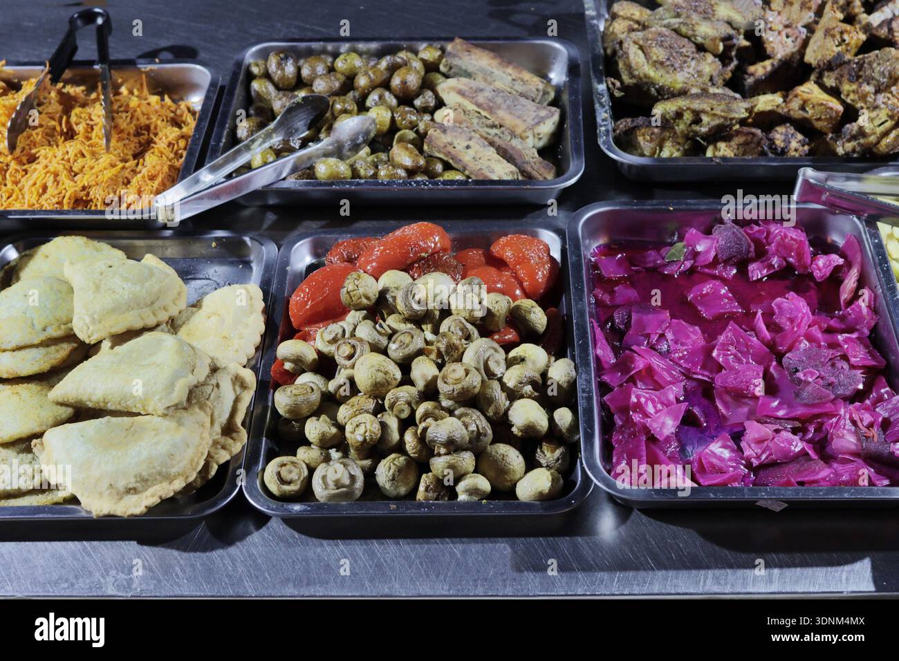 A wide selection of prepared foods on trays and in metal pans – stewed and processed carrots, potatoes, lamb ribs, cutlets, pies, mushrooms, red peppe Stock Photo