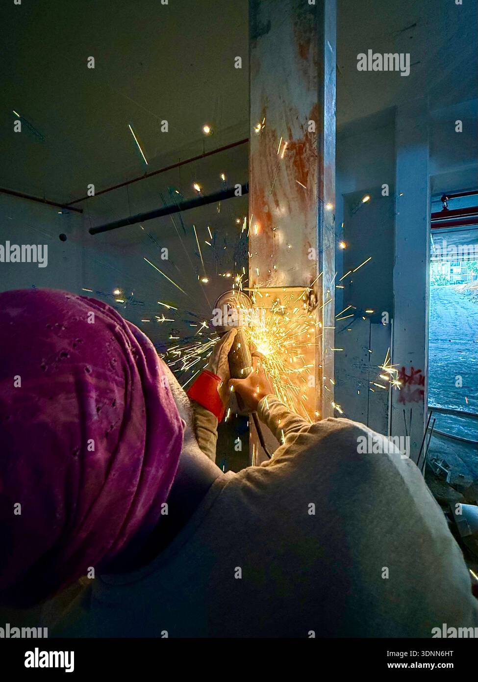 Worker in a pink turban using an angle grinder on a steel beam at a construction site, creating bright yellow sparks in a gritty industrial interior. - Smartphone Captured Stock Image
