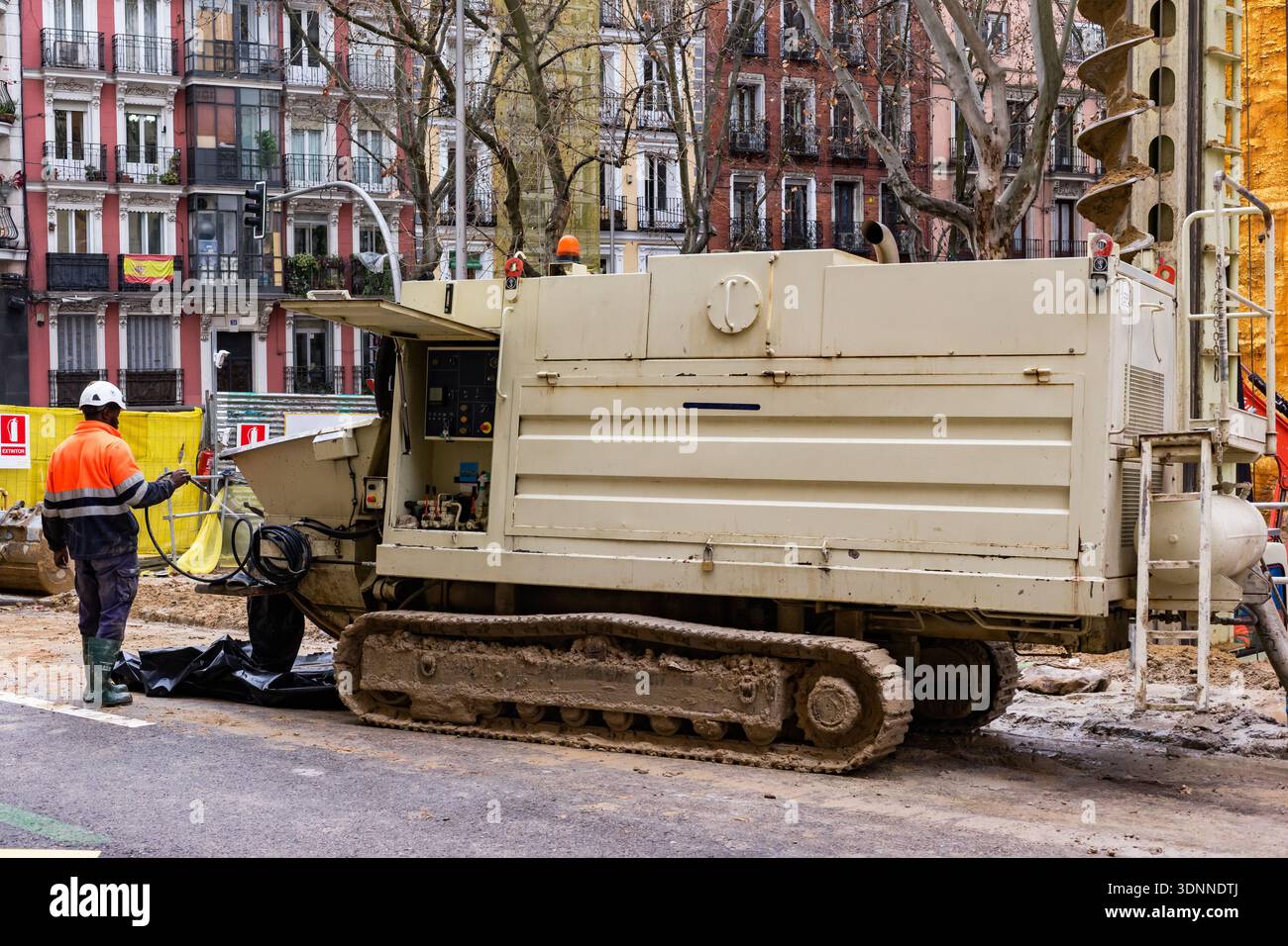 A heavy-duty tracked hydraulic rig stands on an asphalt street during a building renovation project. In the background, traditional apartment balconie Stock Photo