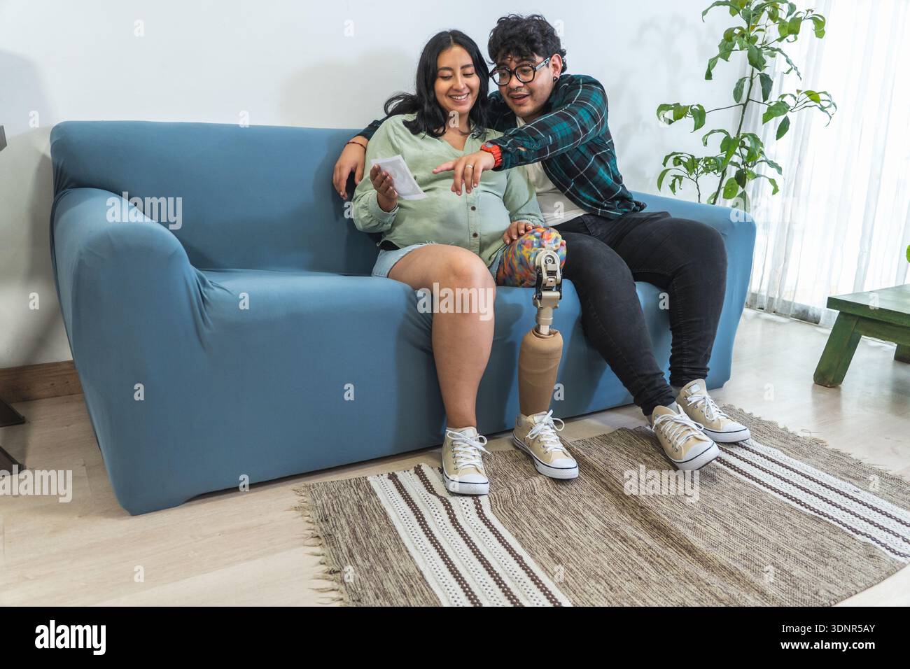 Pregnant woman with prosthetic leg and partner sitting on sofa looking at ultrasound image Stock Photo