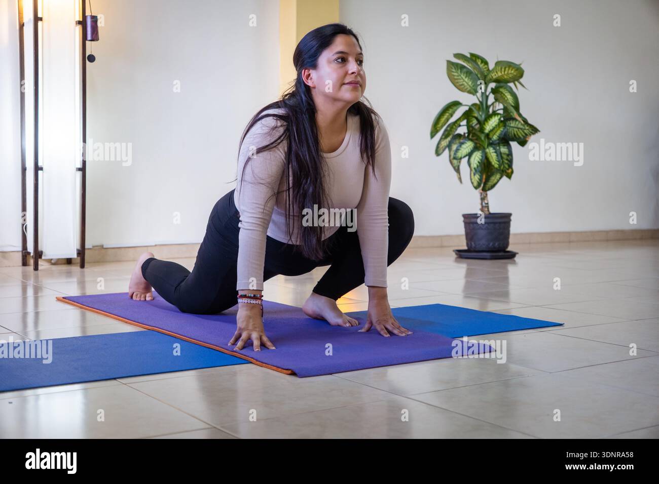 Woman performing a low lunge yoga pose on a mat in a studio Stock Photo ...