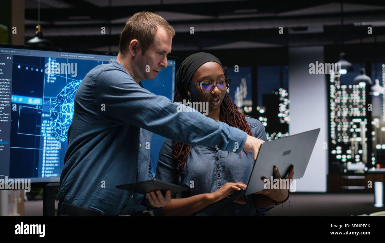 Technicians collaborating to develop artificial intelligence algorithms in high rise office late at night. Tech agency coworkers debug 3D neural network brain models Stock Photo
