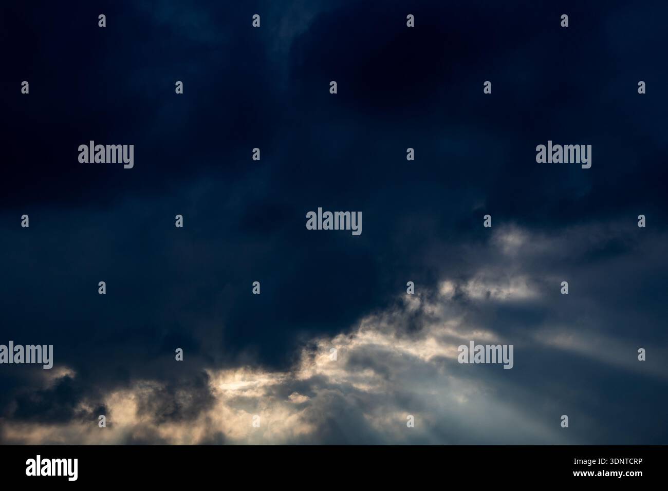 Dramatic sunbeams breaking through dark storm clouds Stock Photo