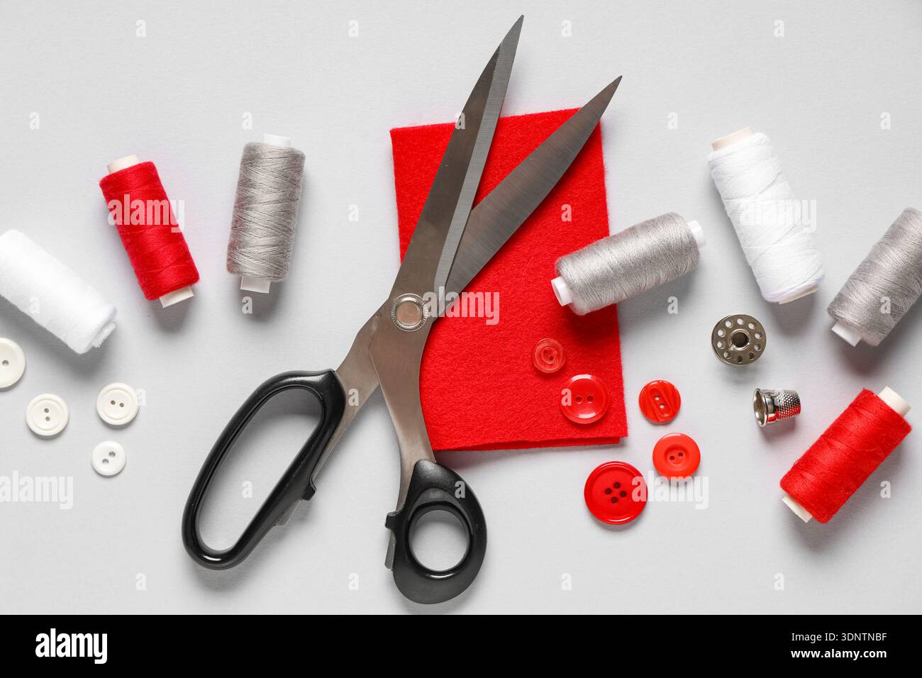 Thread spools with scissors, buttons, fabric and thimble on grey background Stock Photo