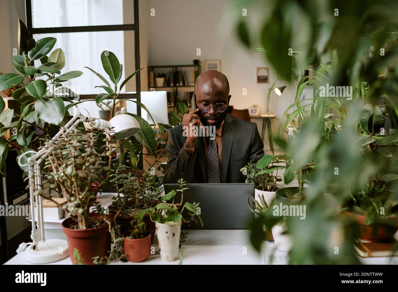 Black Man Working on Laptop and Talking on Smartphone in Office Stock Photo
