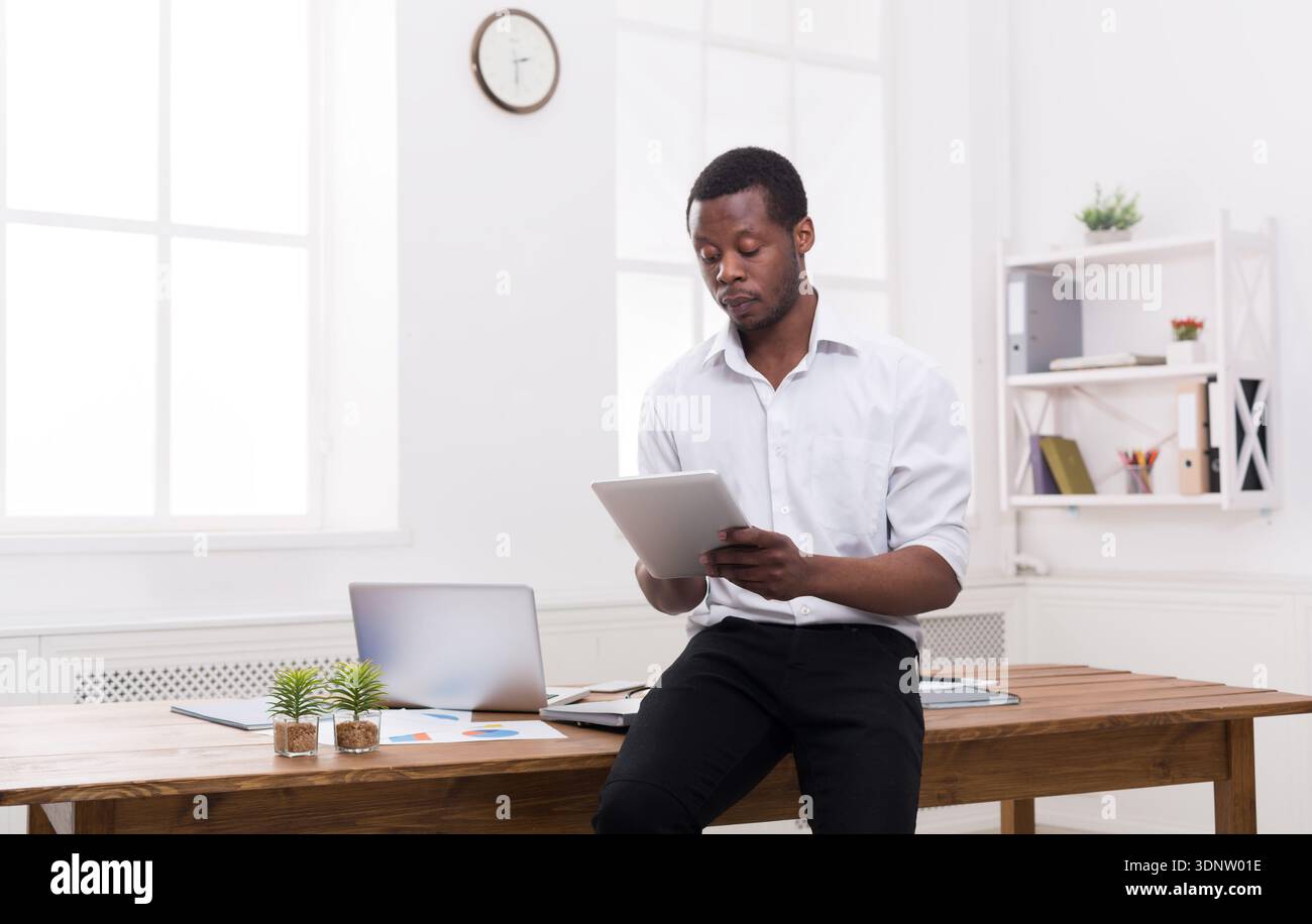 Serious black businessman in modern office, work with tablet Stock Photo