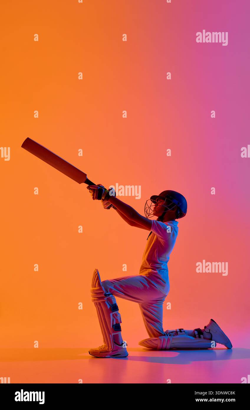 Cricket player kneeling raising bat upward in dramatic gradient light ...