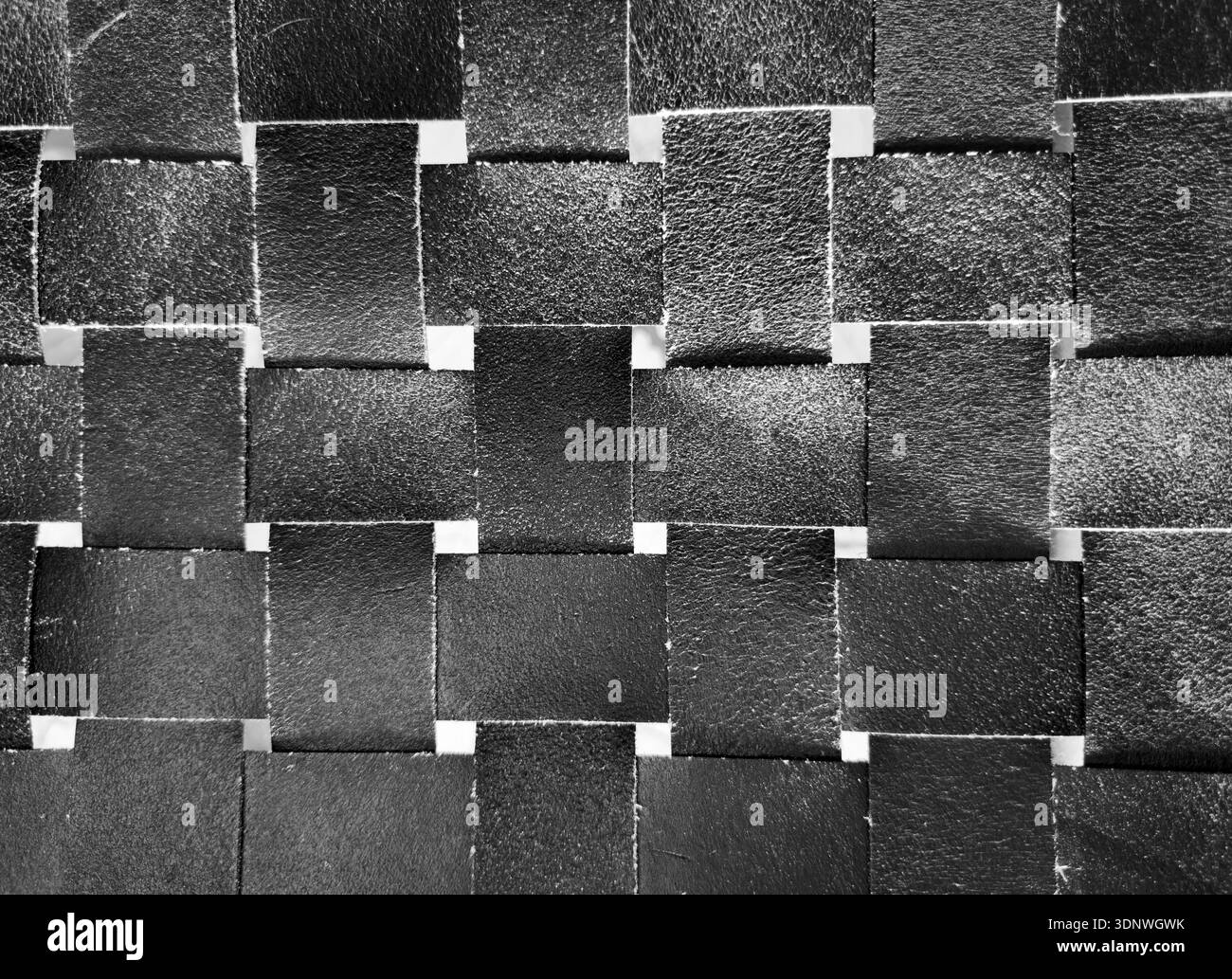 Woven black leather squares create geometric textured surface. Interlaced matte strips form seamless background pattern. Stock Photo