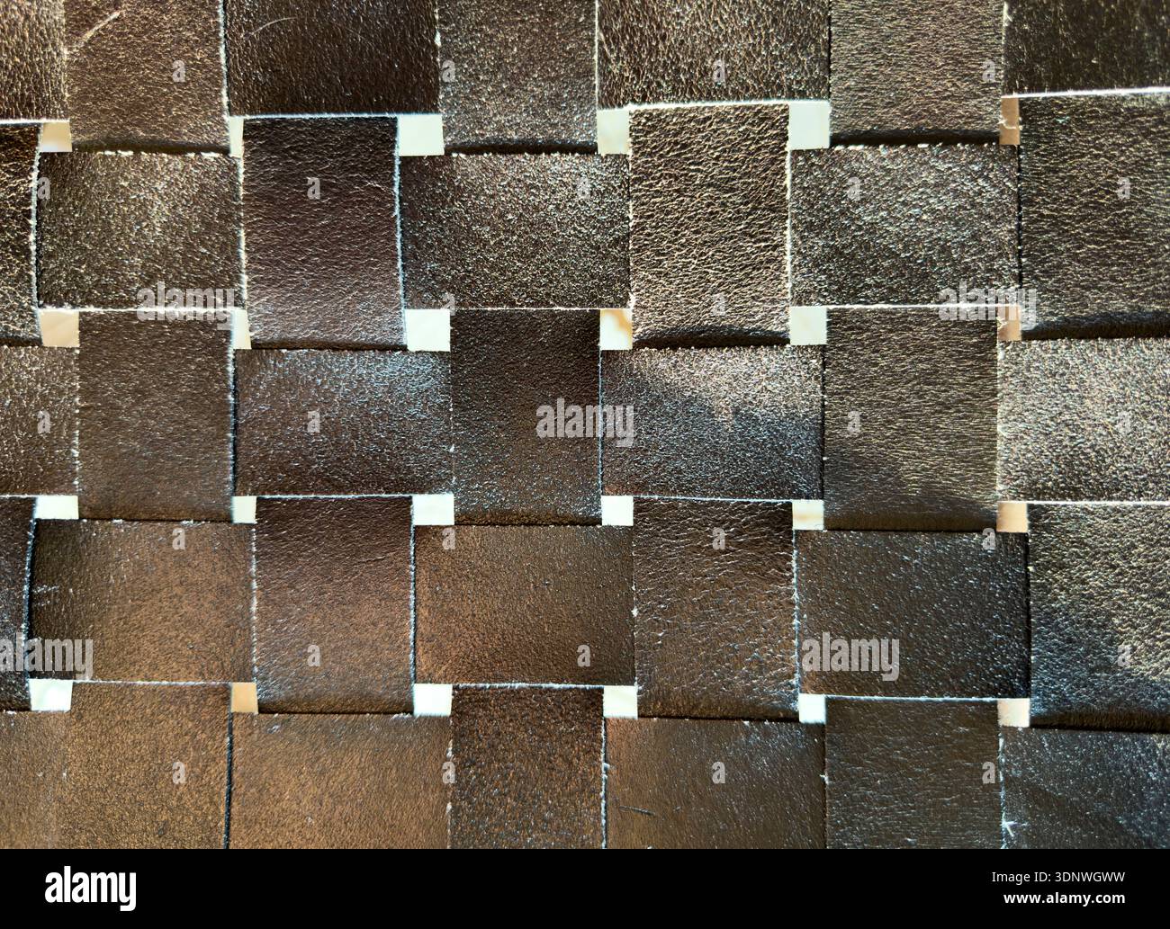 Woven leather squares form geometric grid texture. Interlaced dark strips create seamless background surface. Stock Photo