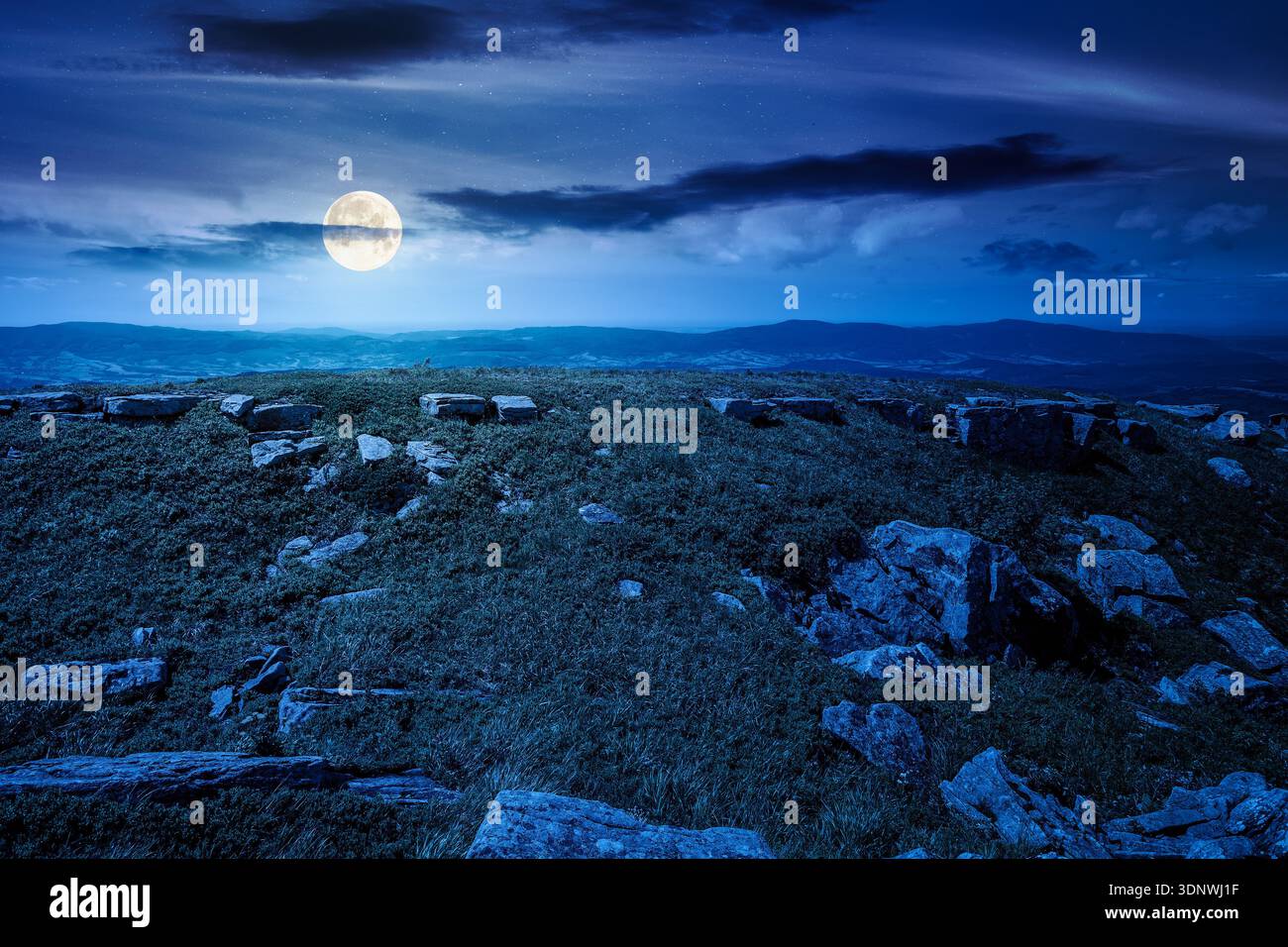 grassy alpine meadow in carpathian mountain landscape at night. sharp rocks and huge boulders among lush grass on rolling hills in full moon light. op Stock Photo
