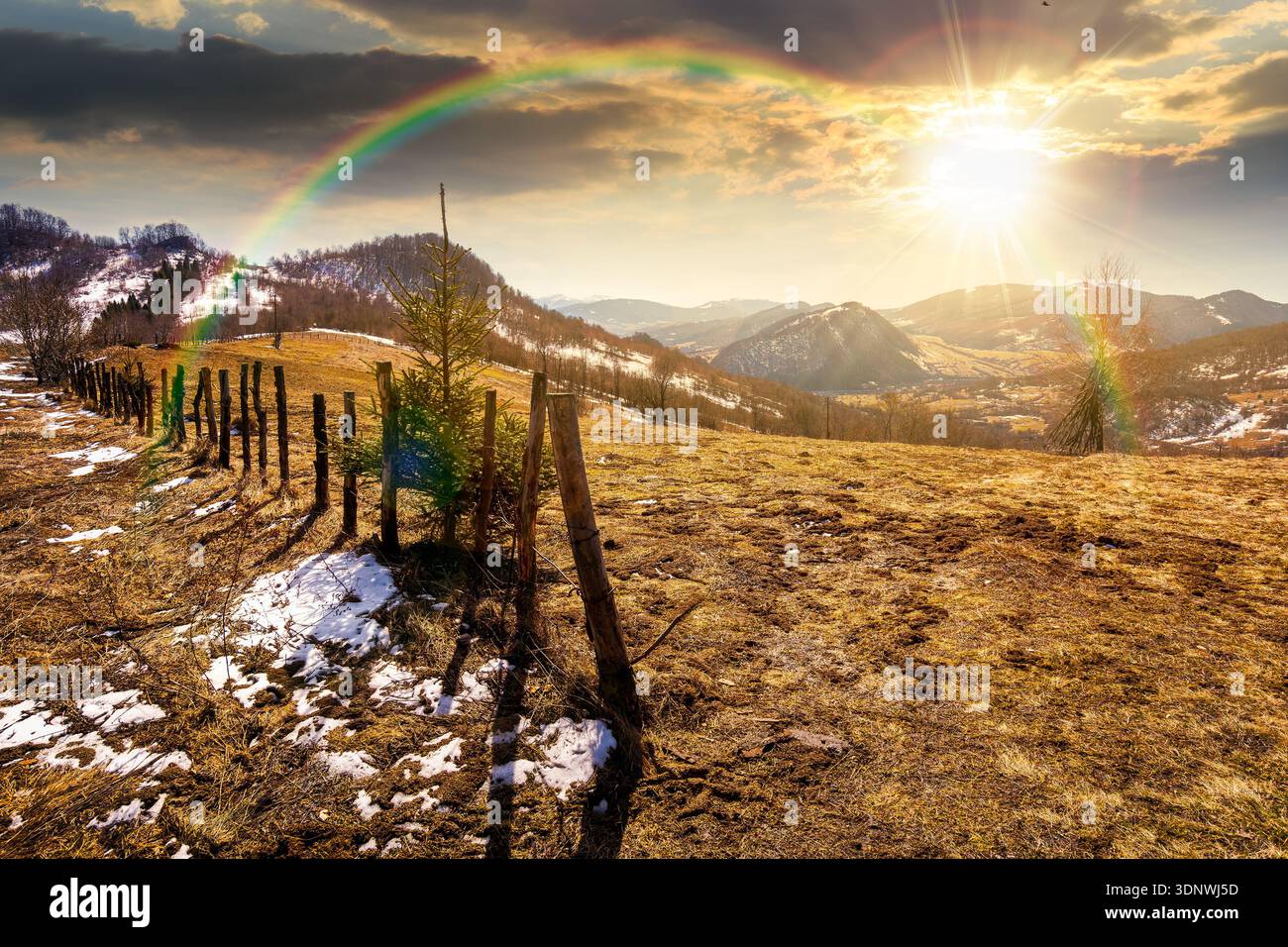 rural landscape of carpathian mountains in early spring under blue sky at sunset. snow covered hill with barbed wire fence on in evening light. storyt Stock Photo