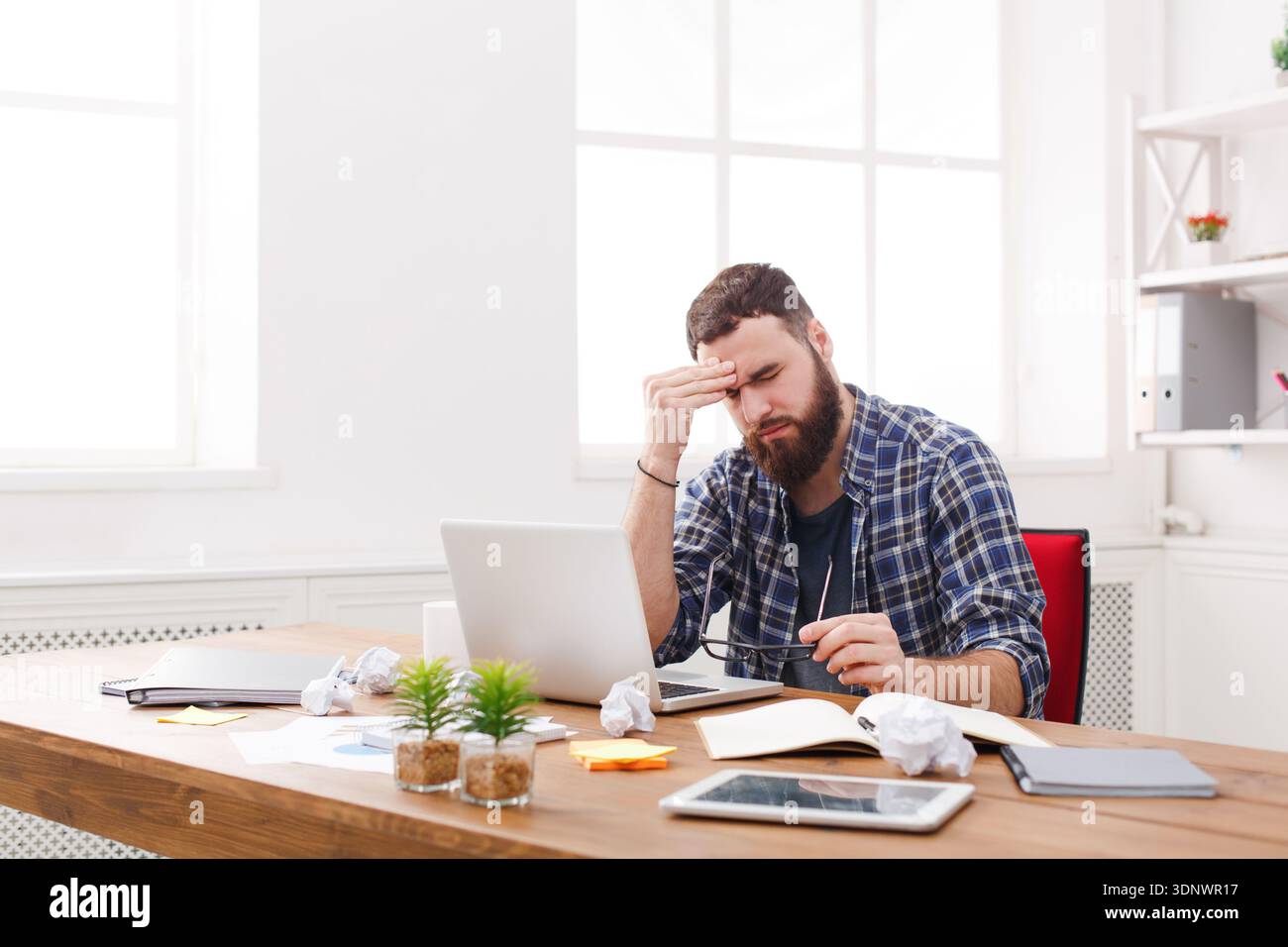 Tired stressed male programmer with laptop in modern white office Stock Photo