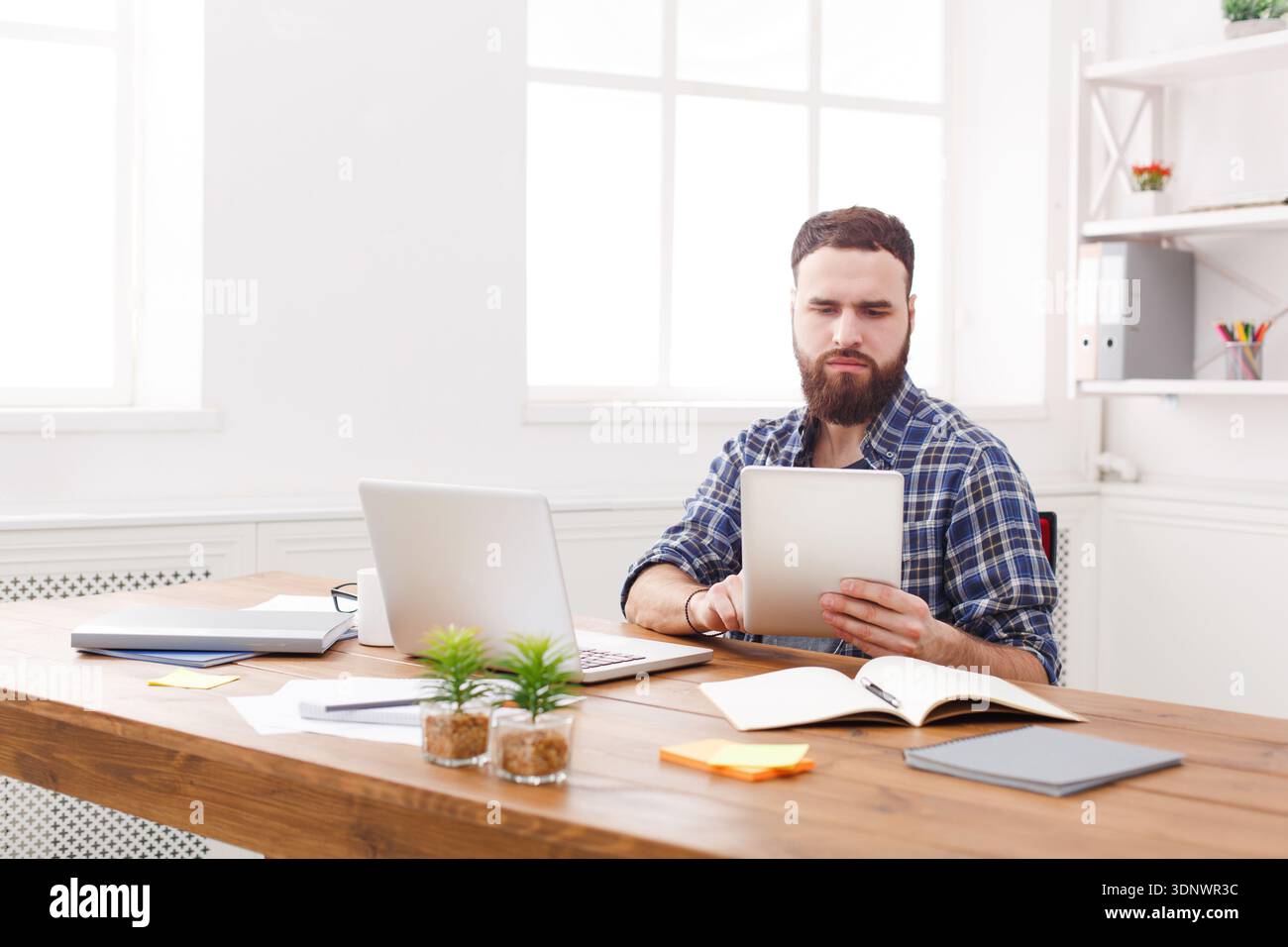 Young concentrated man using tablet at the table with laptop Stock Photo