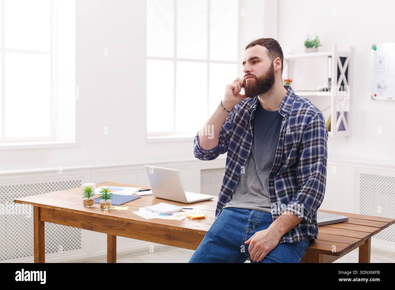 Pensive young businessman talking on mobile phone sits on the table Stock Photo