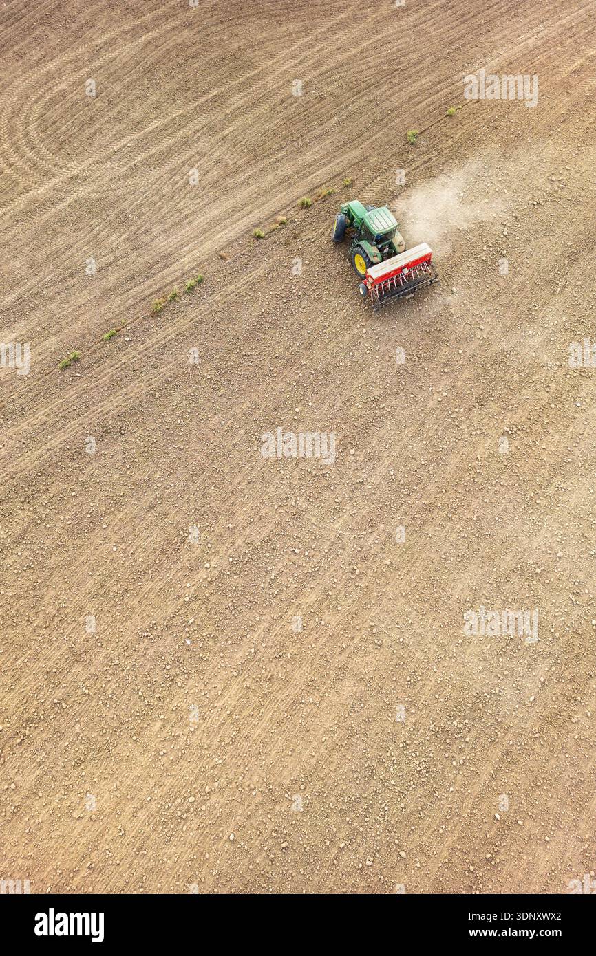 Aerial view of a green tractor plowing an expansive field. The freshly ...