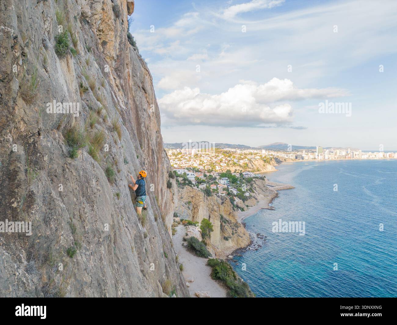 A climber wearing a helmet and harness ascends a vertical cliff face ...