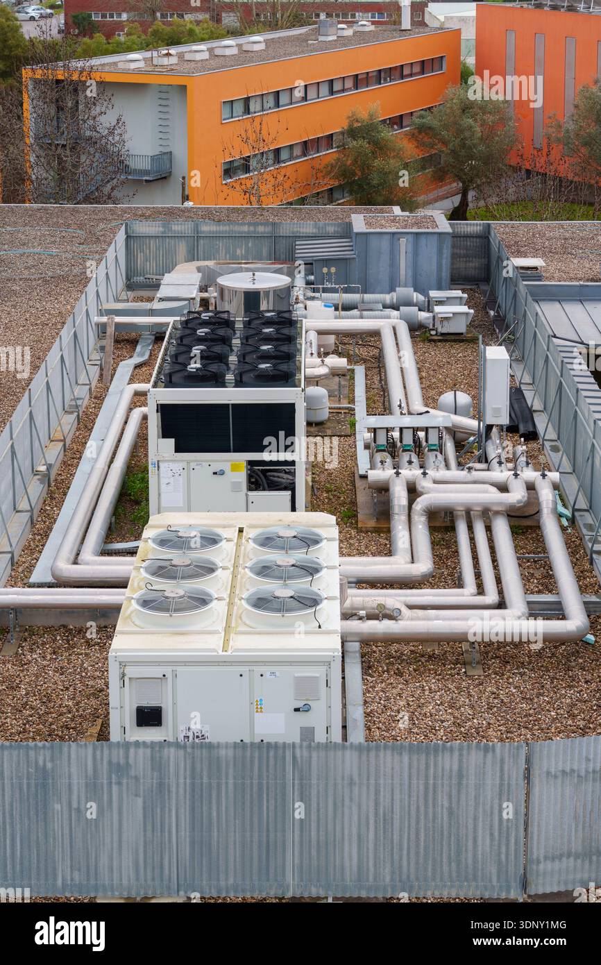 Industrial rooftop HVAC system featuring air conditioning units and a complex network of insulated pipes on a gravel surface Stock Photo