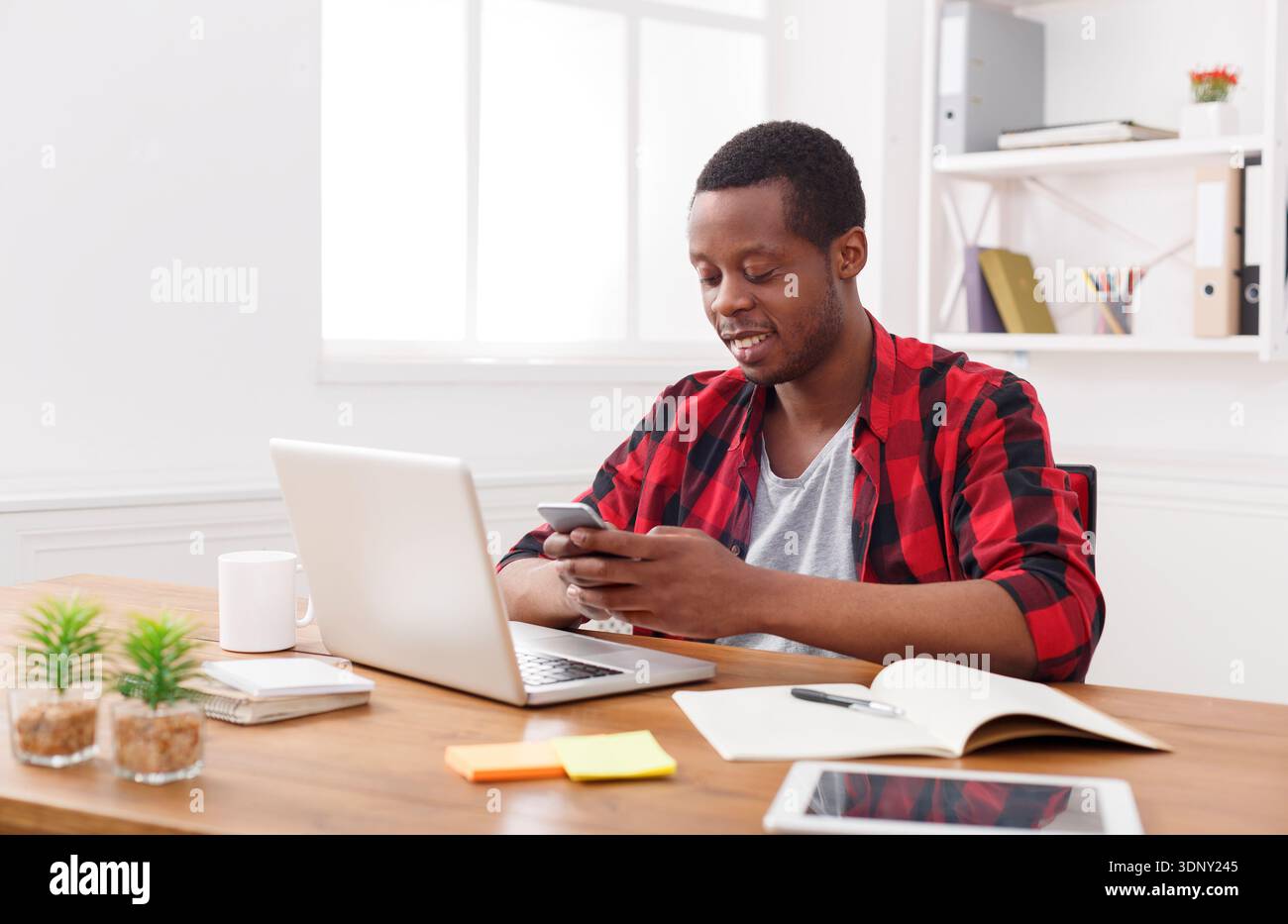 Happy black businessman in office at workplace with mobile Stock Photo