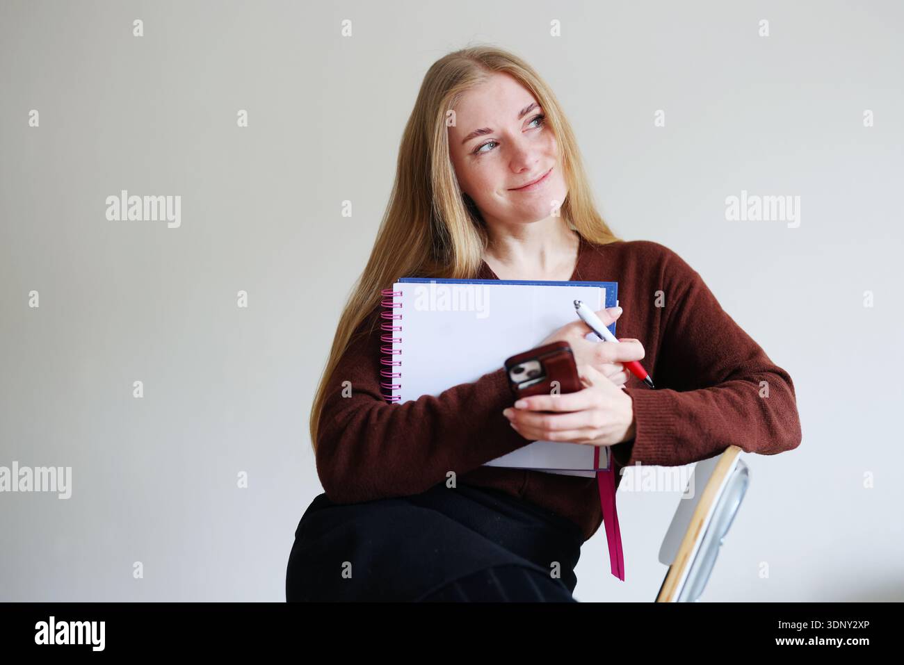 Female freelancer organizing tasks with notebook and phone. Work planning, time management and personal organization concept. Stock Photo