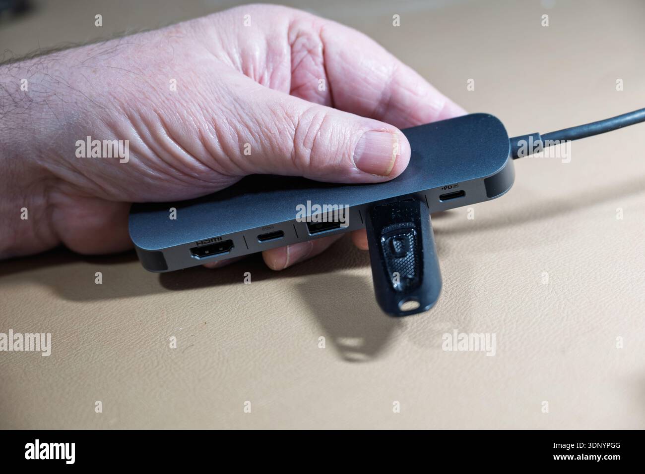 A hand inserts a USB drive into a multi-port adapter, likely for data transfer or device connectivity. Stock Photo