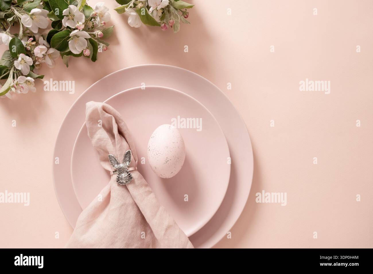 Minimal pastel Easter table composition with decorated egg and linen napkin with silver bunny ring on plate. Stock Photo