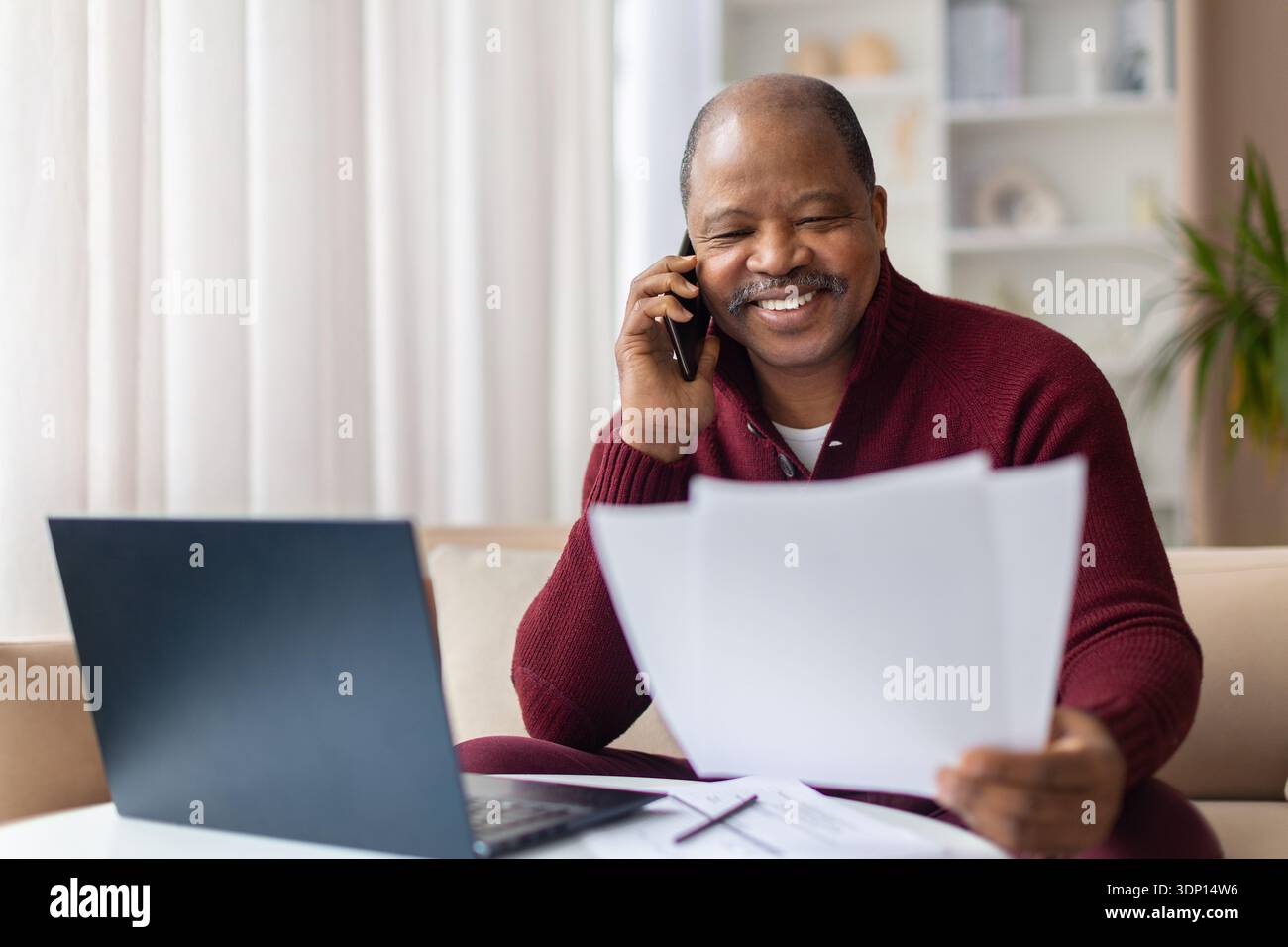 Mature black man talking on smartphone while checking documents at home Stock Photo
