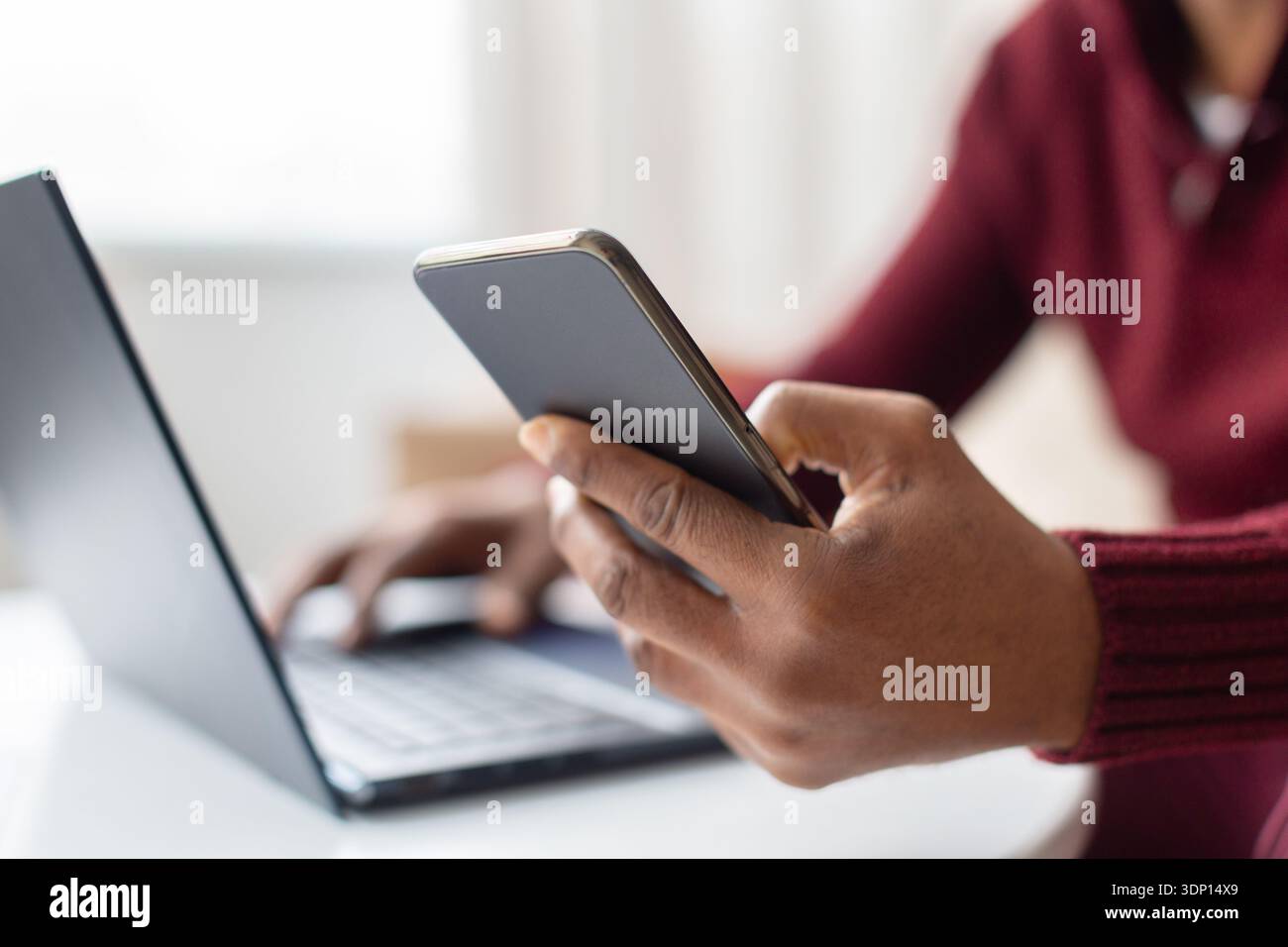 Middle aged black man using smartphone while working on laptop at home Stock Photo