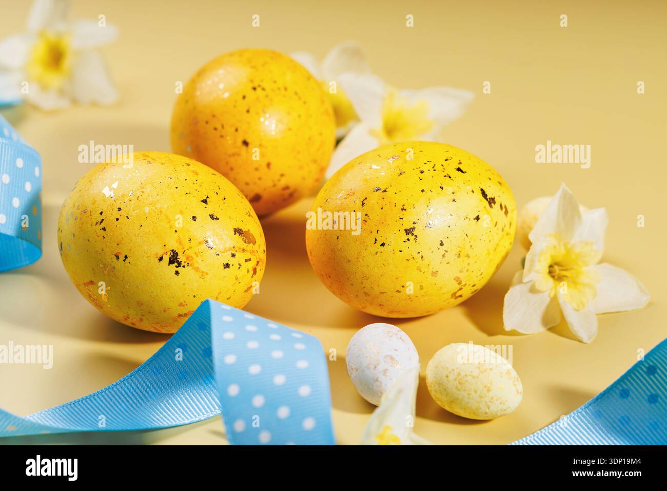 Speckled Easter eggs and spring flowers on beige surface Stock Photo