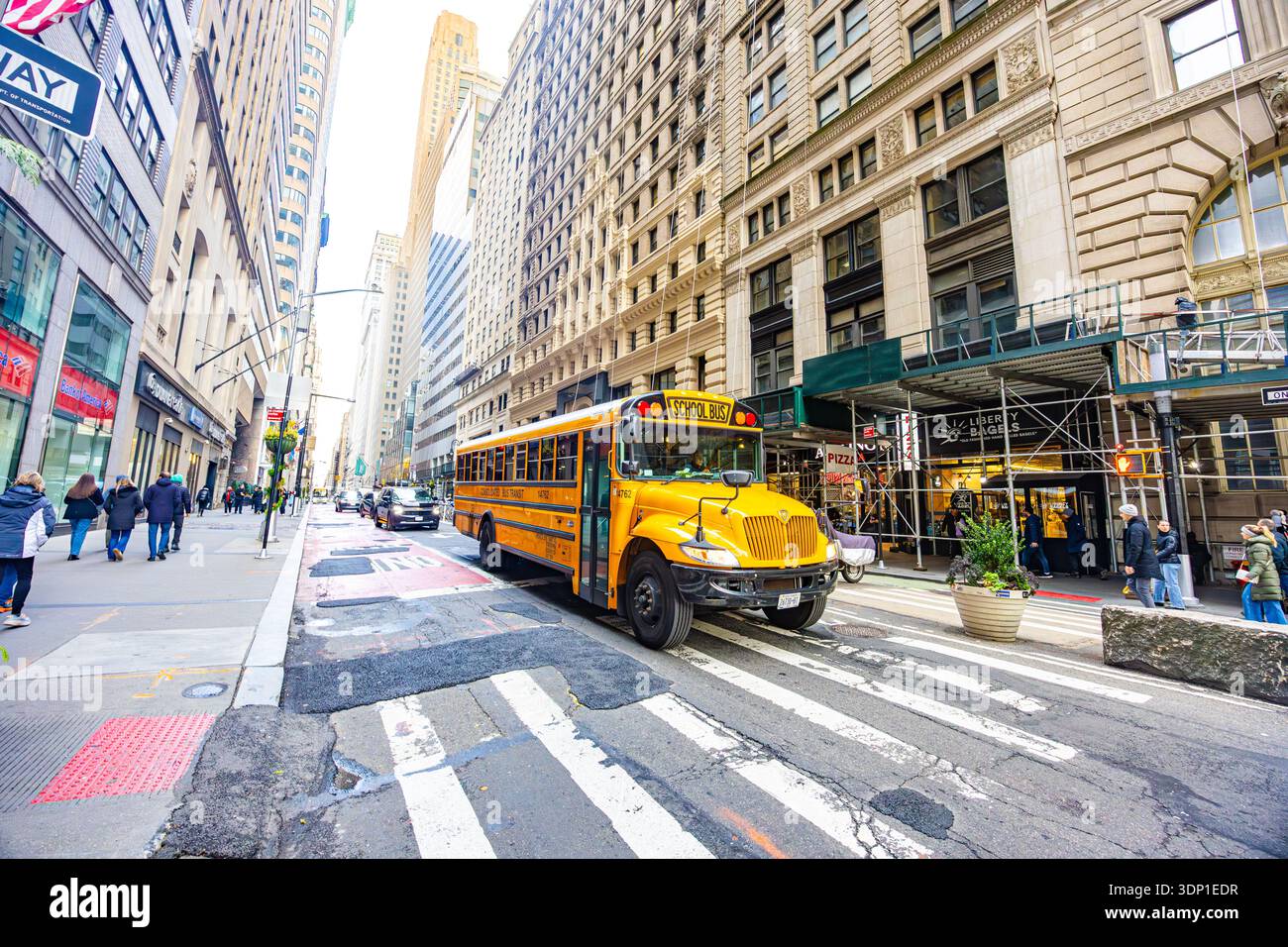 Yellow school bus driving through Manhattan street with pedestrians traffic and historic office buildings in downtown New York Stock Photo