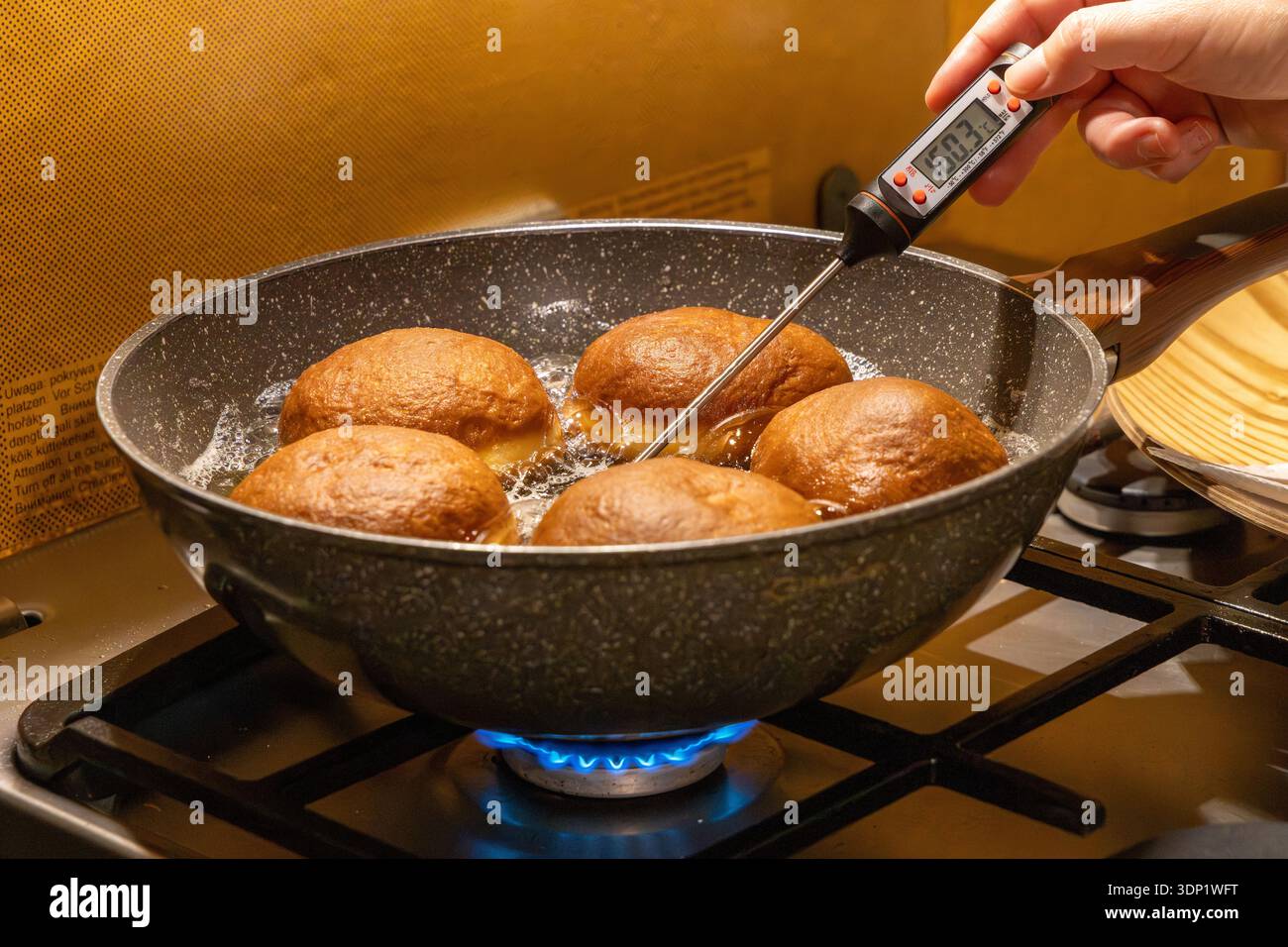 Measuring oil temperature with digital probe thermometer while frying golden doughnuts on gas stove for perfect traditional dessert preparation. Stock Photo