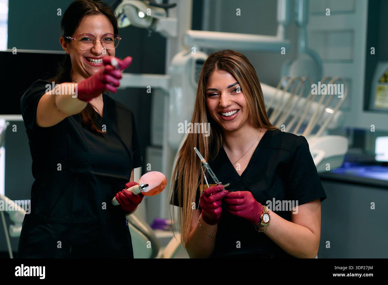 Two Friendly Dental Assistants Share a Laugh While Preparing Tools in Modern Clinic Stock Photo