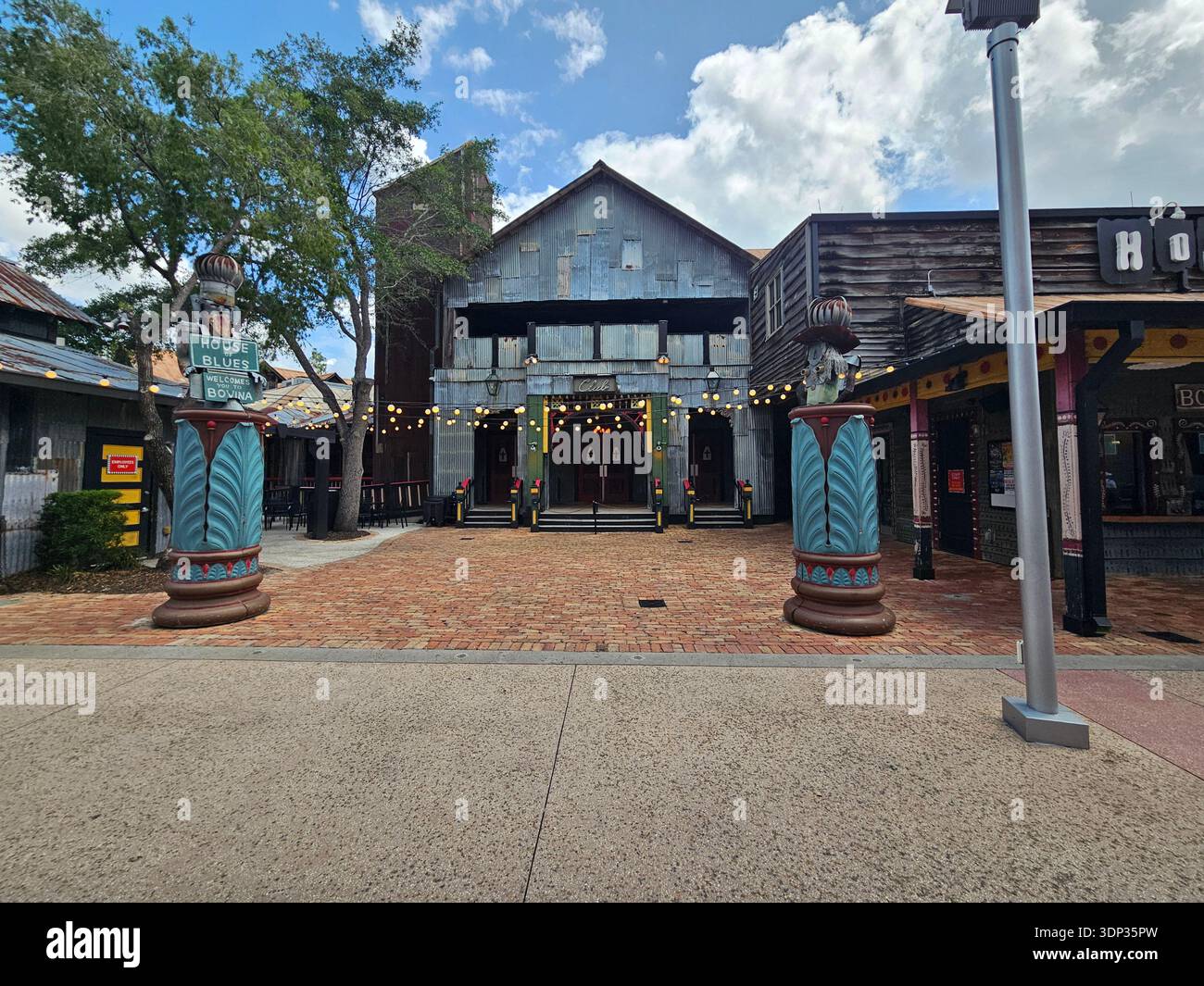 EDITORIAL USE ONLY- ORLANDO FLORIDA: ​The entrance to the House of Blues Music Hall at Disney Springs, Orlando, Florida. The building features a rustic, eclectic "juke joint" design with corrugated metal siding, folk art sculptures, and a brick-paved courtyard under a bright sky. - Smartphone Captured Stock Image