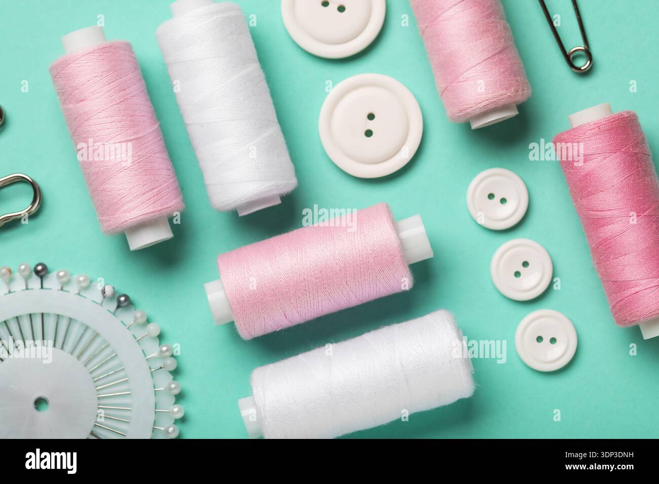 Composition with thread spools, ball pins and buttons on mint background, closeup Stock Photo
