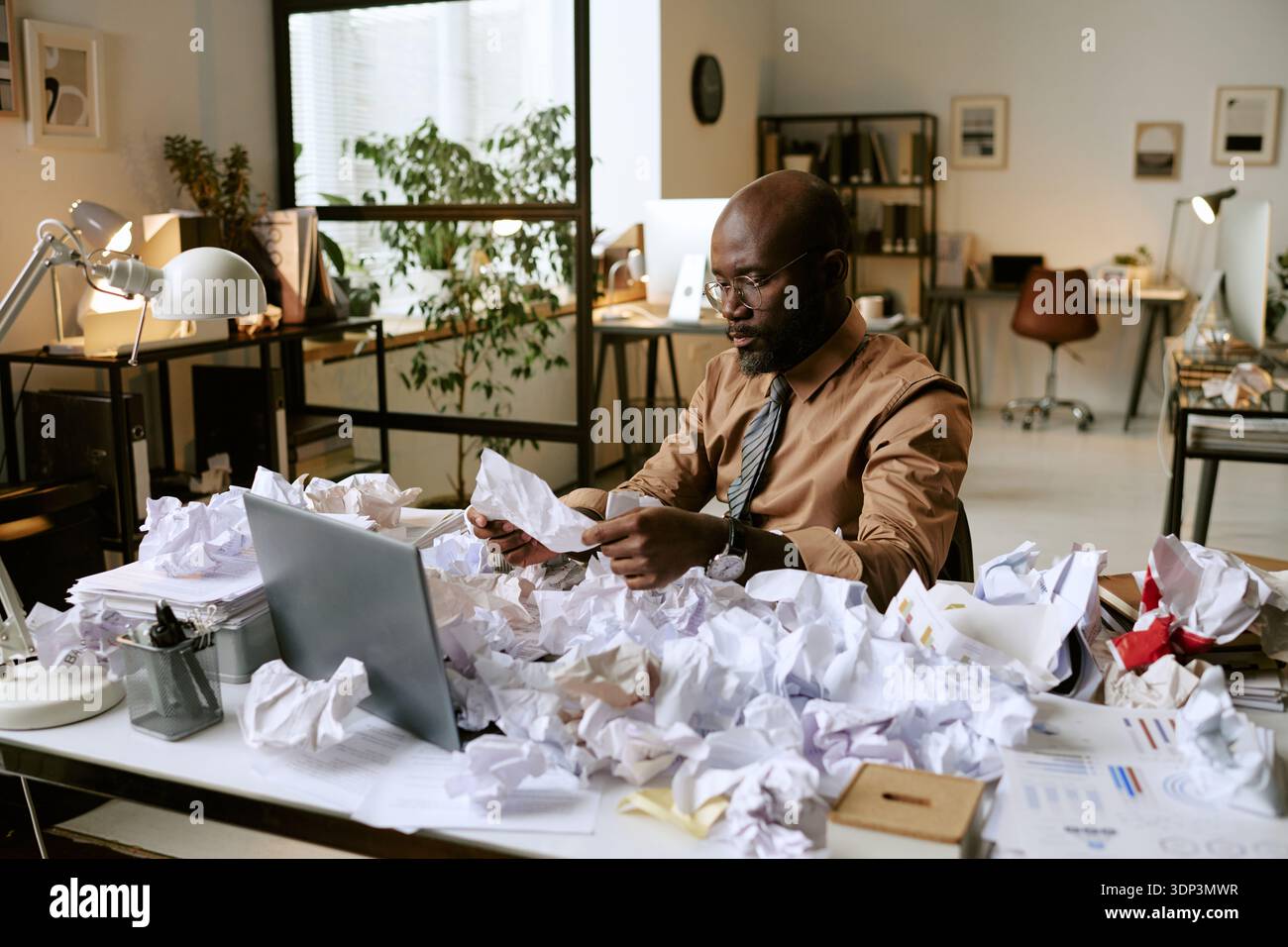 Black Man Analyzing Documents at Desk in Busy Office Environment Stock Photo