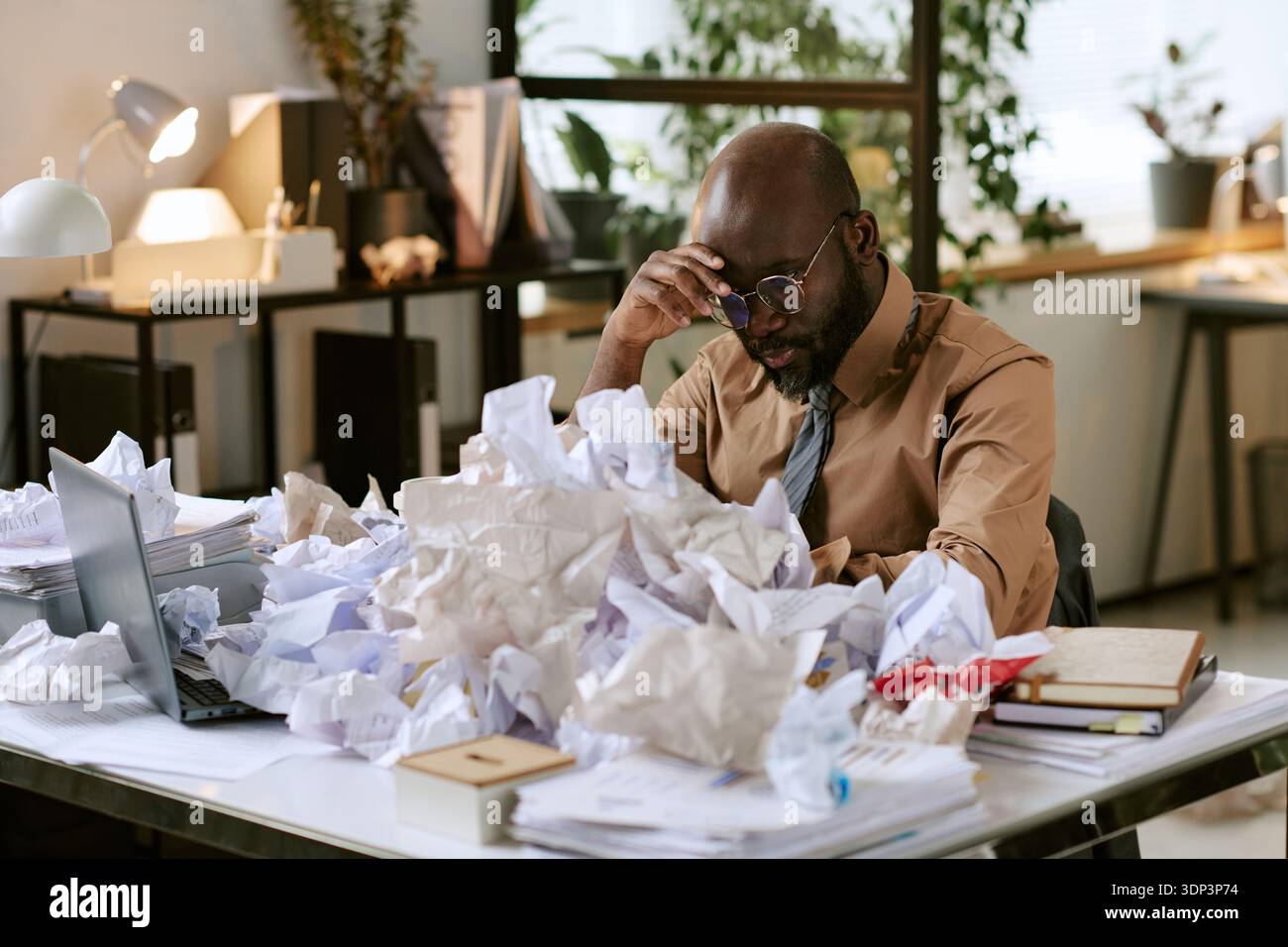 Black Man Sitting at Desk Feeling Stressed in Office Environment Stock Photo