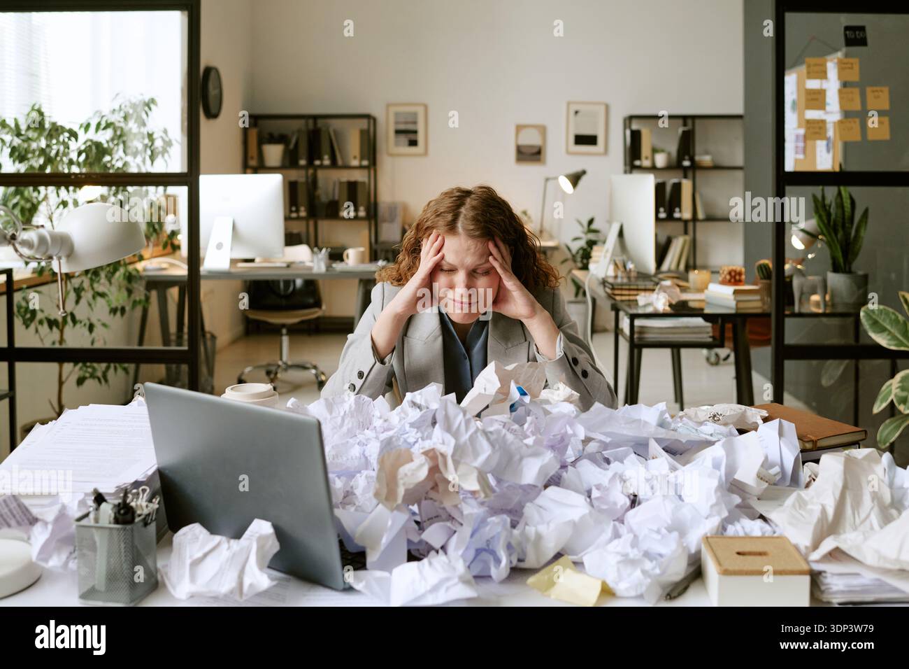 Young Woman Struggling with Paperwork Overload at Office Desk Stock Photo
