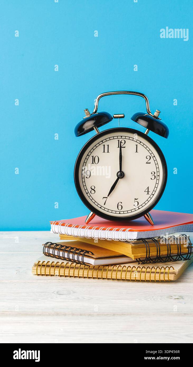 Clock sits on notebooks against a blue backdrop during daytime in a study area Stock Photo