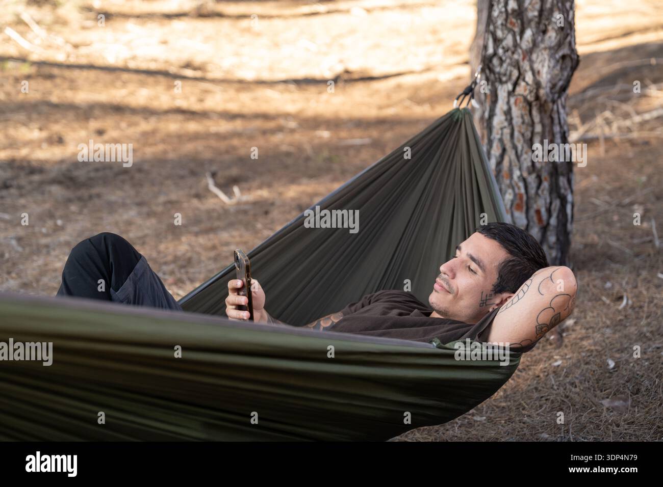 Man relaxing in hammock using smartphone in nature Stock Photo