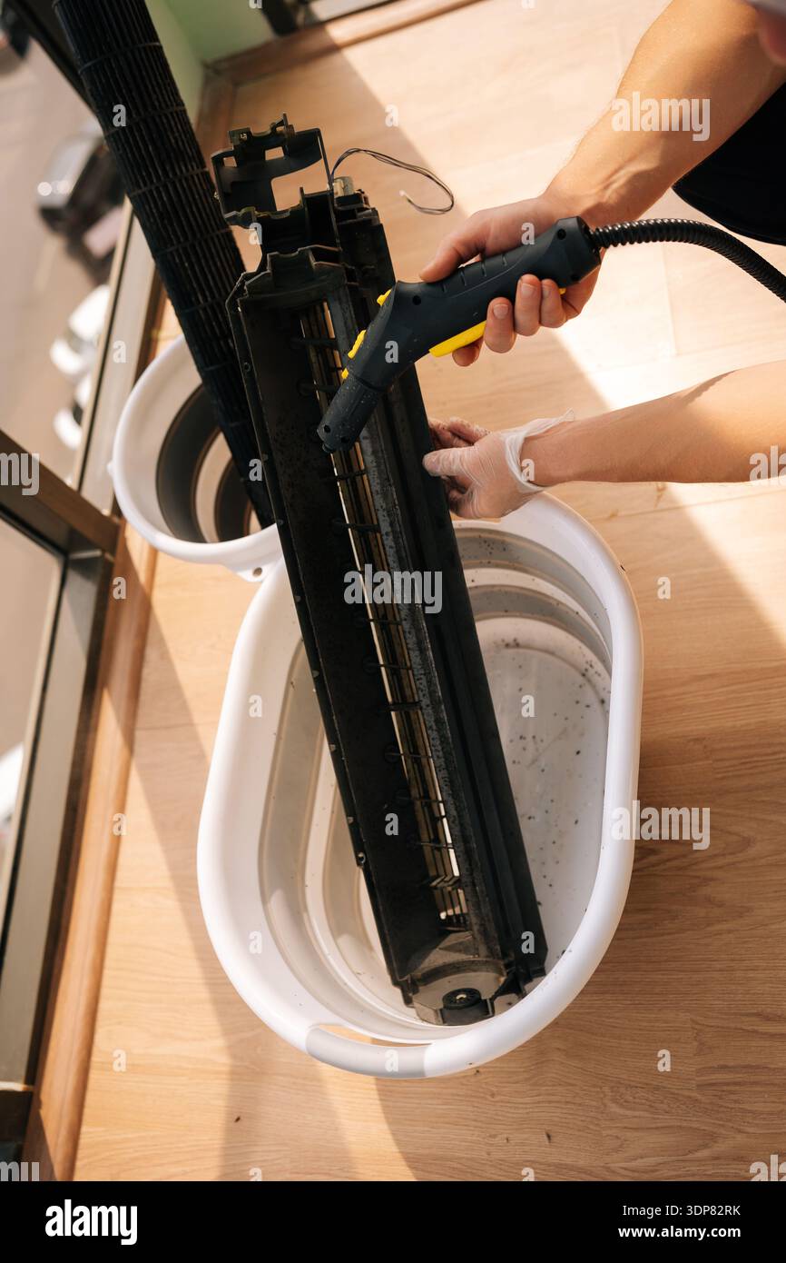 High-angle view of unrecognizable cleaning service employee washing air conditioner filter with steam cleaner, focusing on maintenance and cleaning Stock Photo