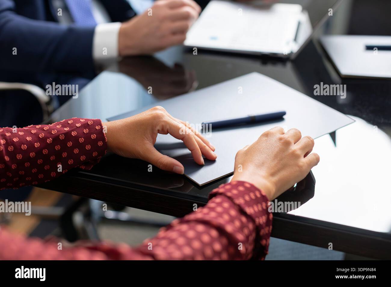 Hands of people are placed on a table covered with documents and a pen. One person has a notepad ready while others engage in conversation. This is a Stock Photo