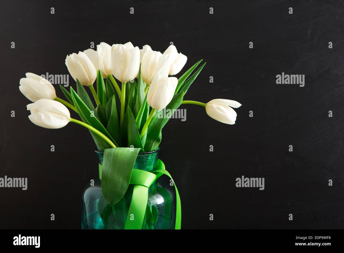 Arrangement of White Tulips in a Green Glass Vase With a Ribbon on a Dark Background Stock Photo