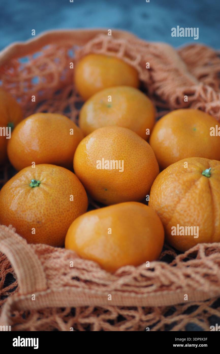 Fresh oranges in a net bag on a blue surface Stock Photo