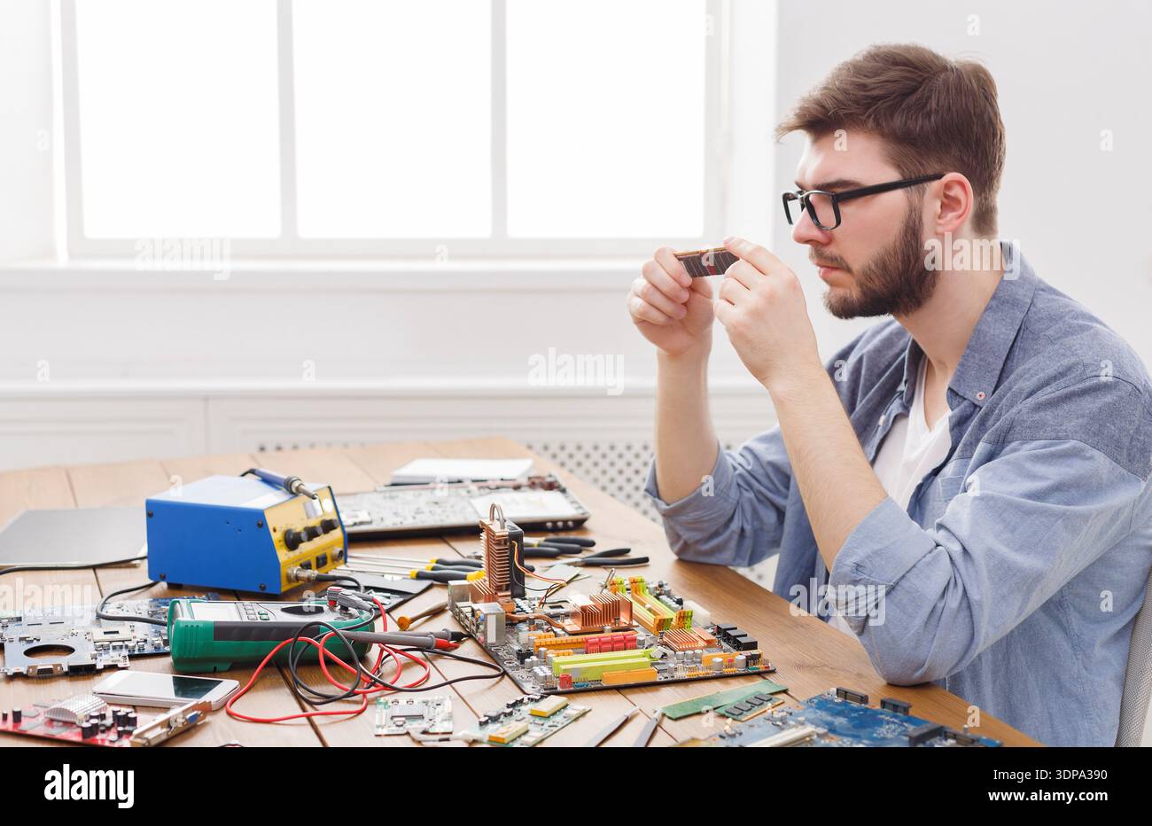 Computer Technician Examines Circuit Board Components in Workshop Setting With Tools Around Stock Photo
