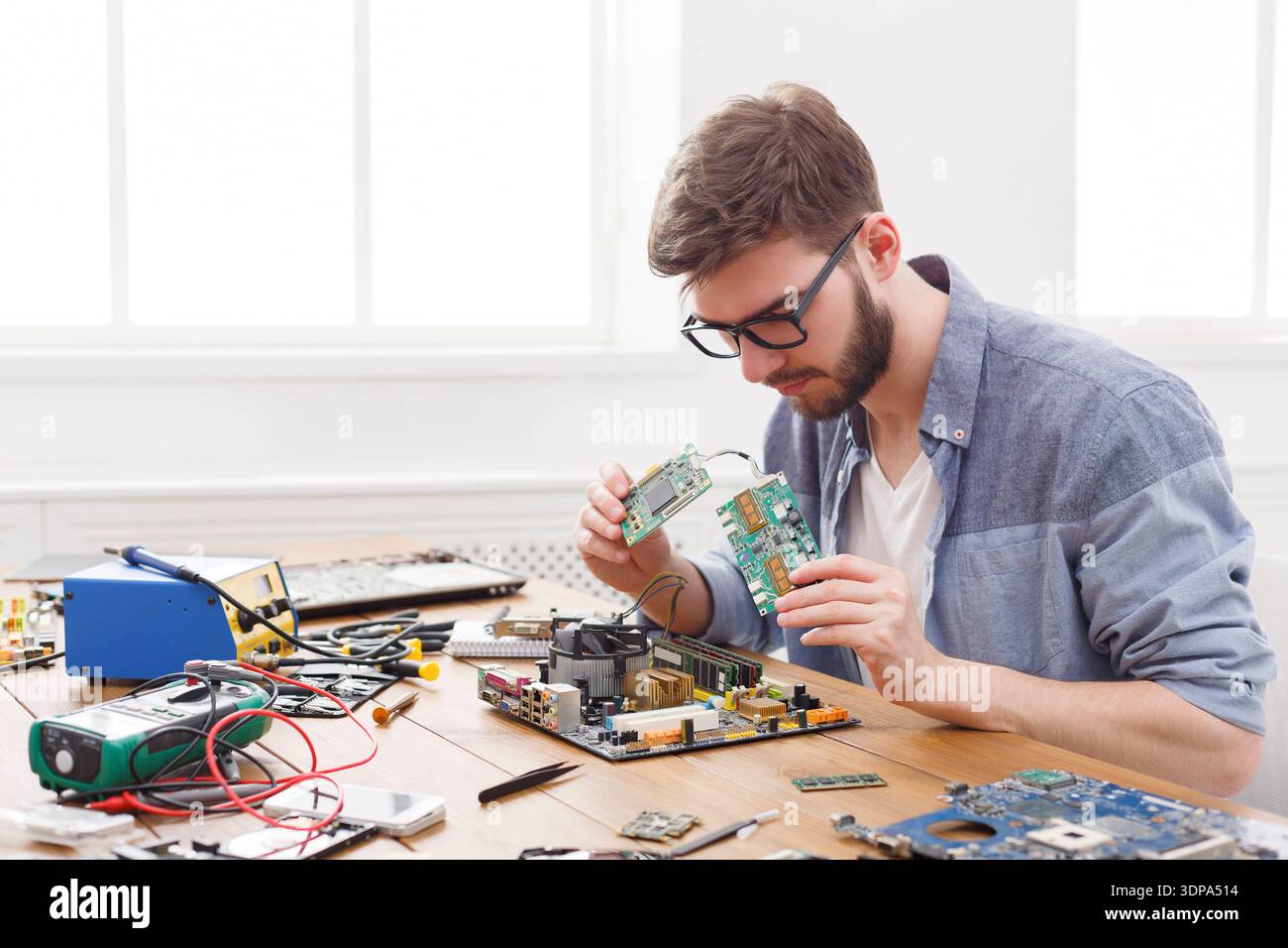 Technician Repairs Circuit Board at Work Table During a Technical Project in a Bright Room Stock Photo