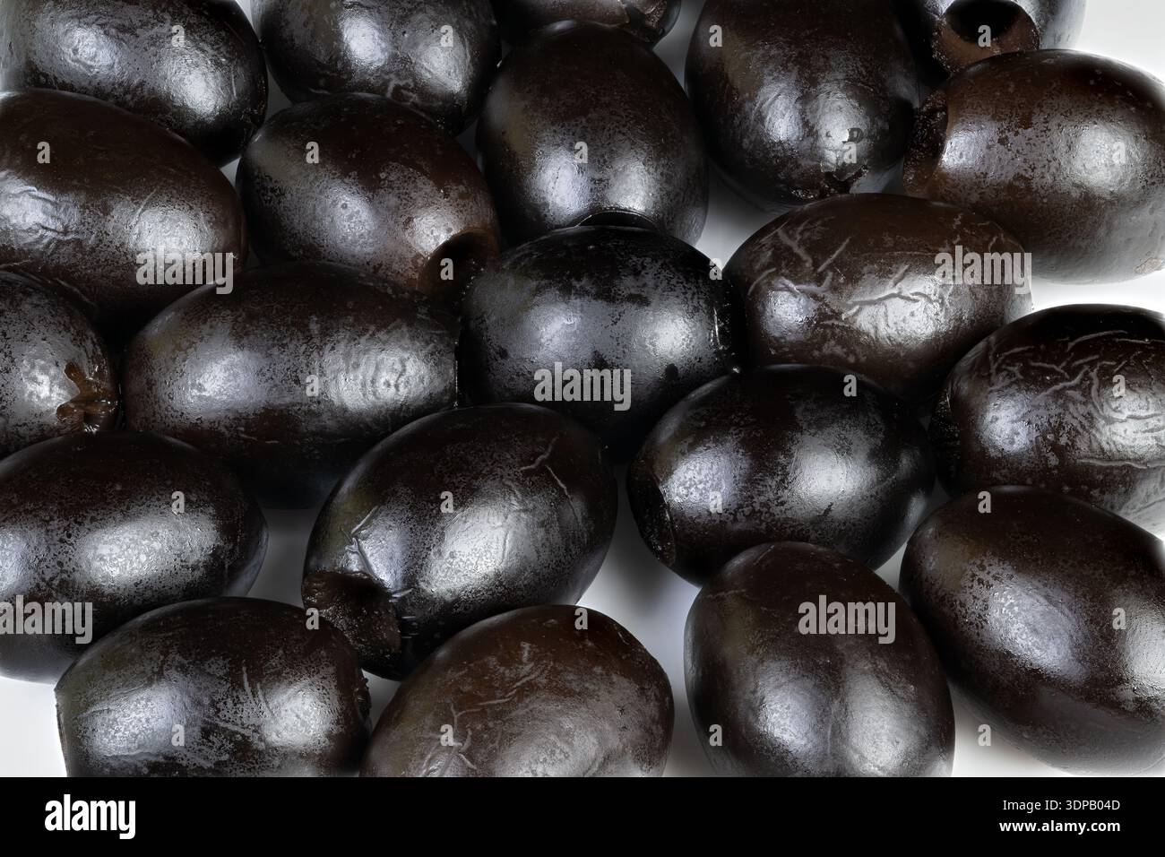 Shiny black olives piled closely on white background, glossy brine sheen, pitted surfaces, chef ingredient for Mediterranean recipes, styled for culin Stock Photo